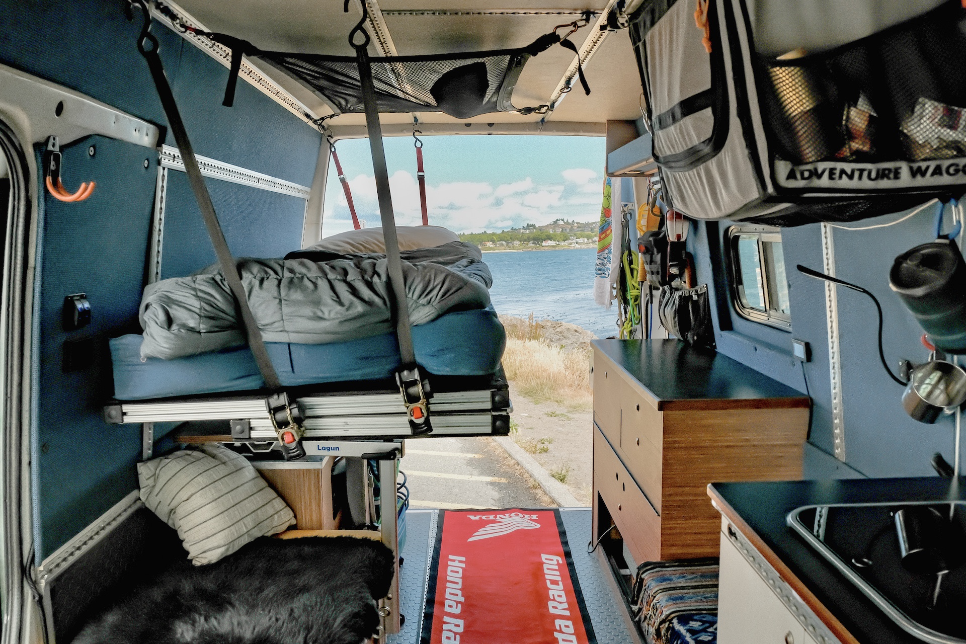 Adventure-ready rv rental camper van interior. Features a bed, kitchen, and open rear doors overlooking the ocean.. Mercedes-Benz Sprinter 2006