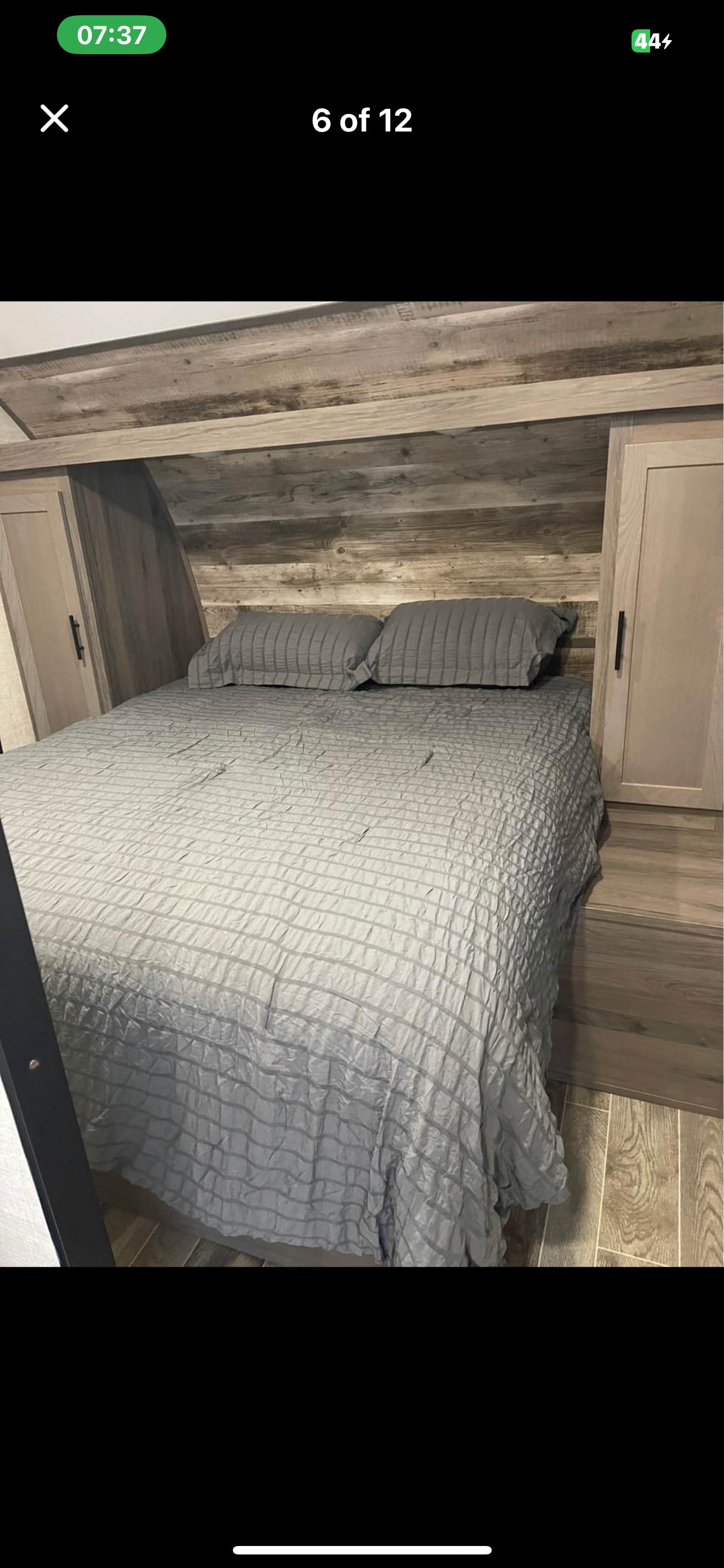 Cozy RV rental bedroom with grey bedding, rustic wood paneling, and built-in storage cabinets.. Gulf Stream Ameri-Lite 2022