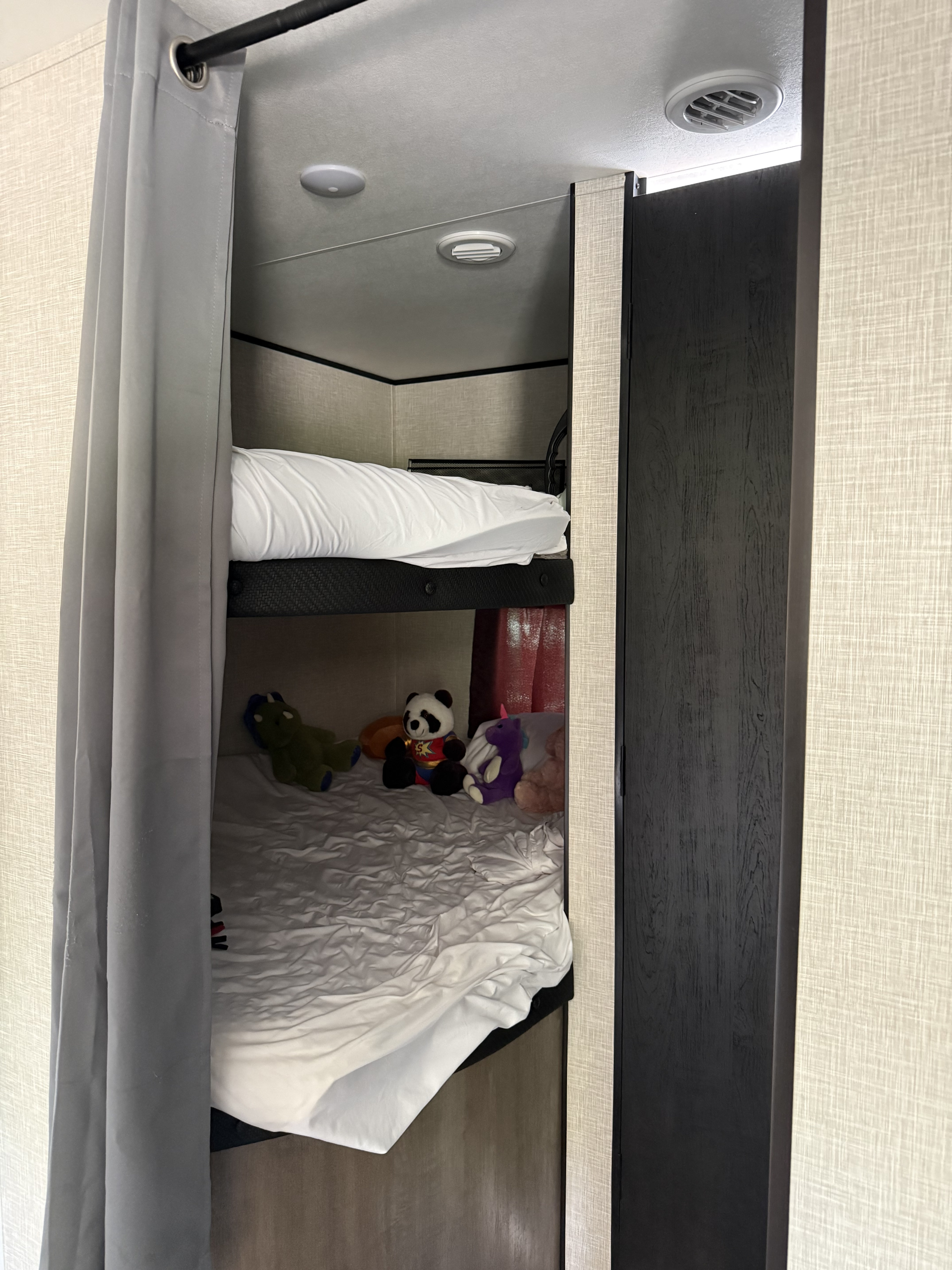 Cozy RV rental bunk beds with a privacy curtain, toys on the lower bunk, ceiling vents, and interior lighting.. Jayco Jay Flight SLX 2024