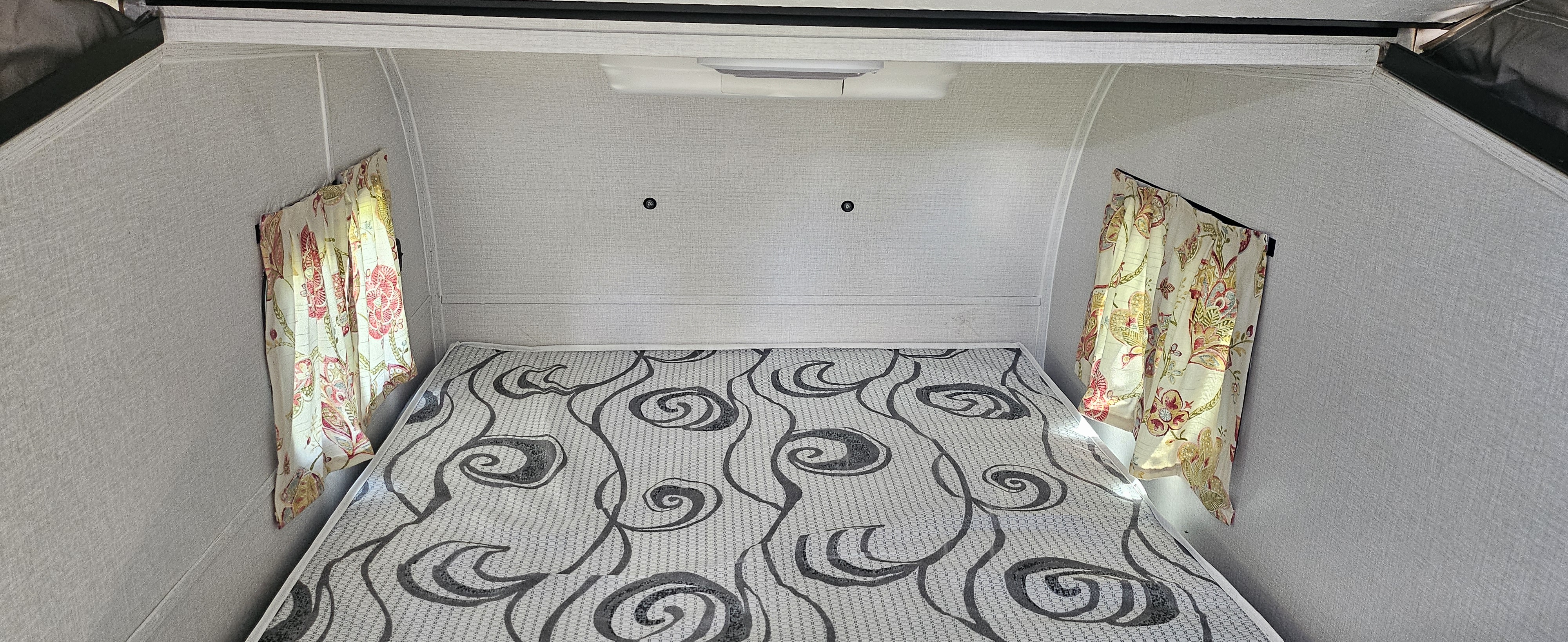 Cozy rv rental sleeping area featuring a patterned mattress, light walls, floral curtains, and overhead lighting.. Coachmen Clipper 2022