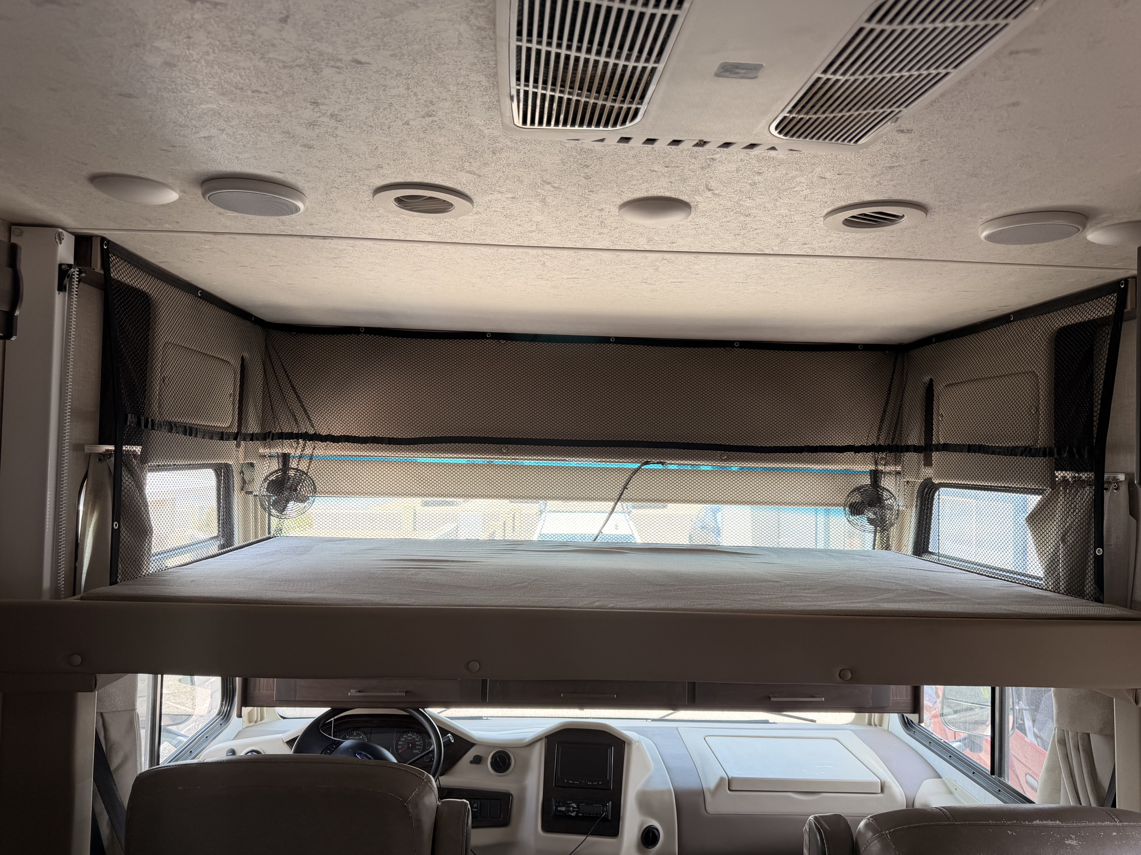 RV rental interior: large over-cab bunk bed with safety net and fans, dashboard, ceiling AC vents, and speakers.. Coachmen Mirada 32SS 2019