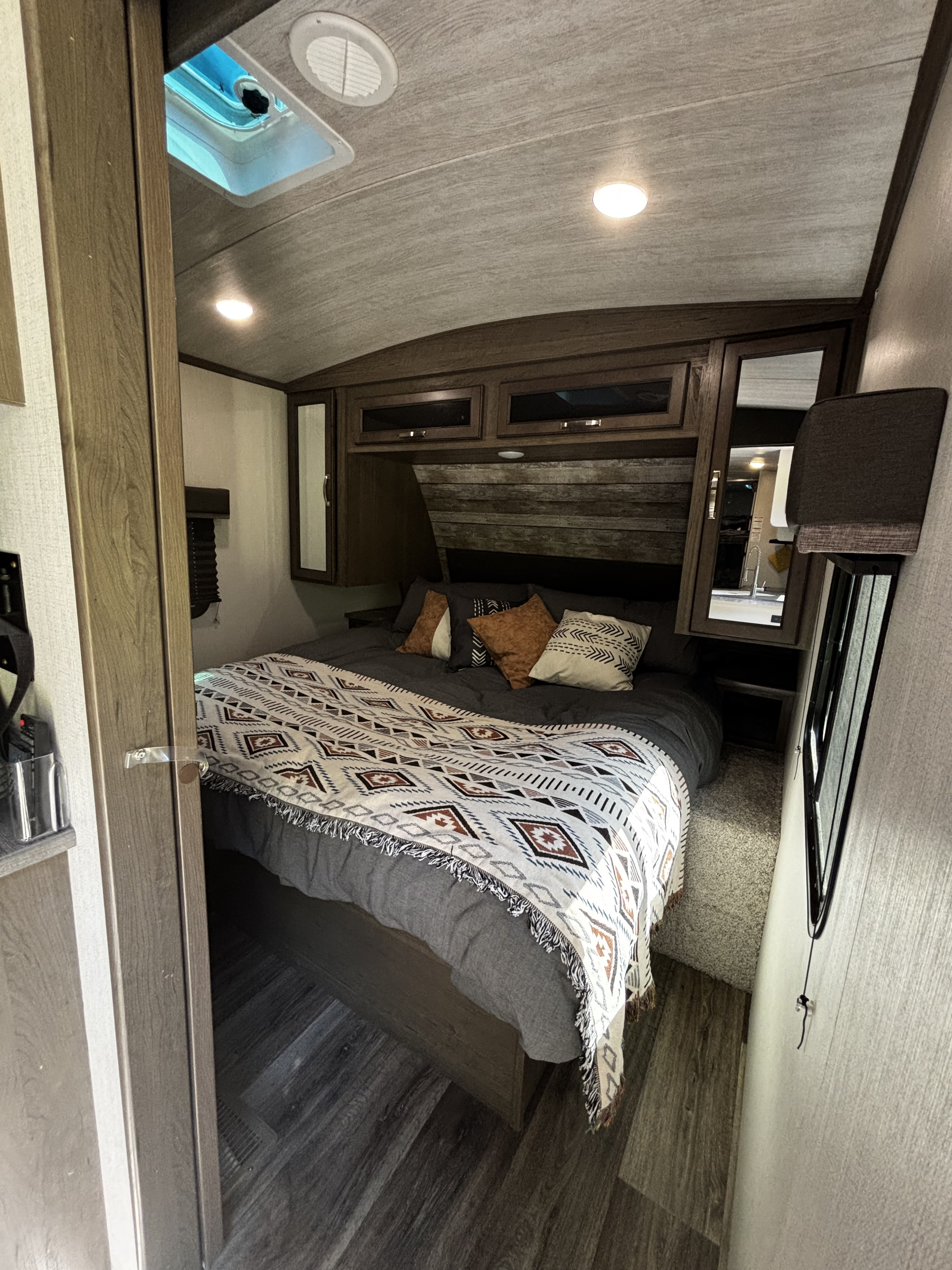 Cozy RV rental bedroom interior with a comfortable bed, decorative blanket, wood accents, overhead storage, and ceiling vent.. Keystone RV Cougar 2021