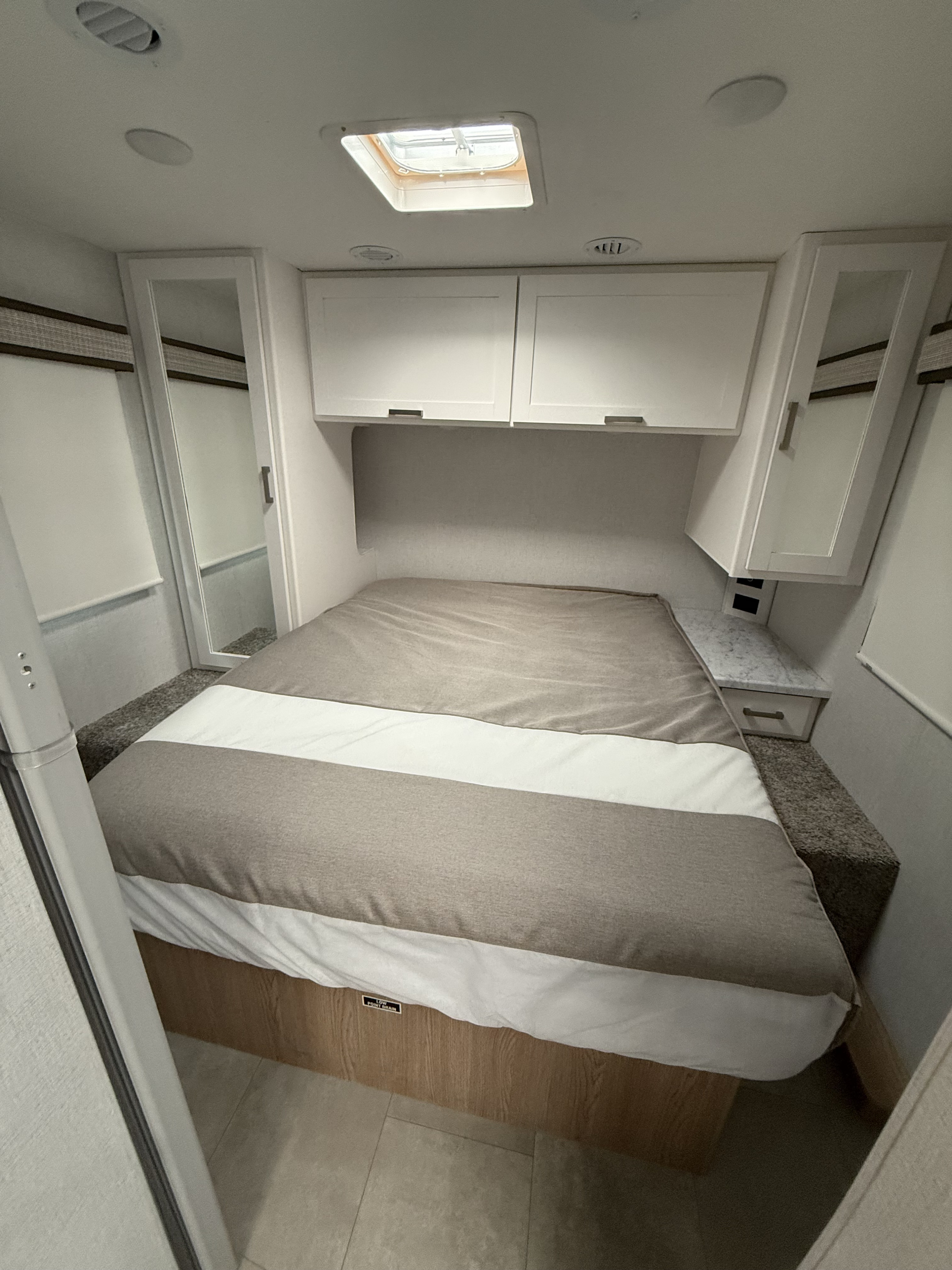 This RV rental bedroom features a bed, white overhead cabinets, side storage units, and a ceiling skylight, perfect for adventurers.. Thor Freedom Elite 2026
