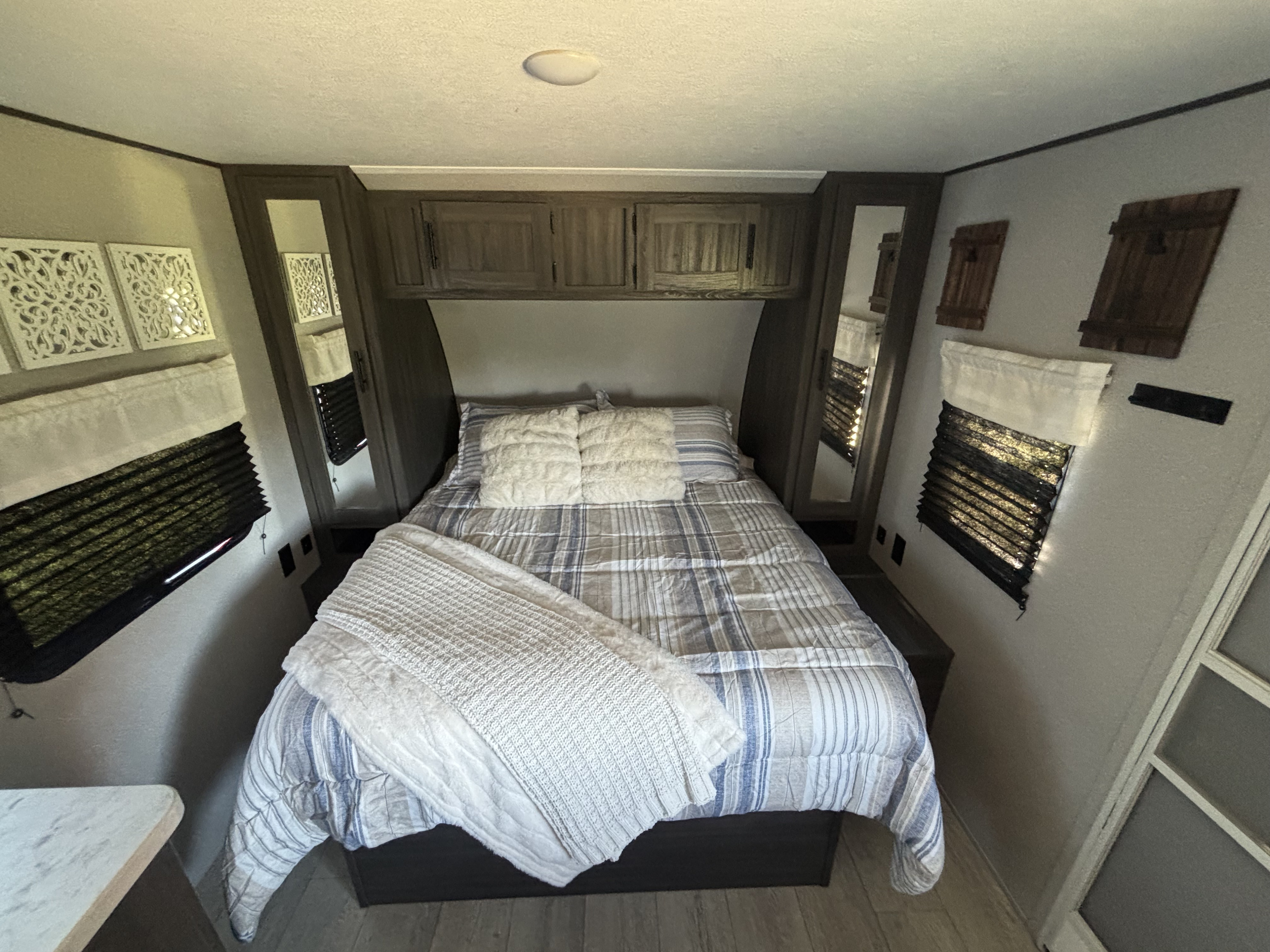 Relax in this cozy RV rental bedroom featuring a striped bed, overhead cabinets, windows with blinds, and rustic decor.. Forest River Shasta 2021