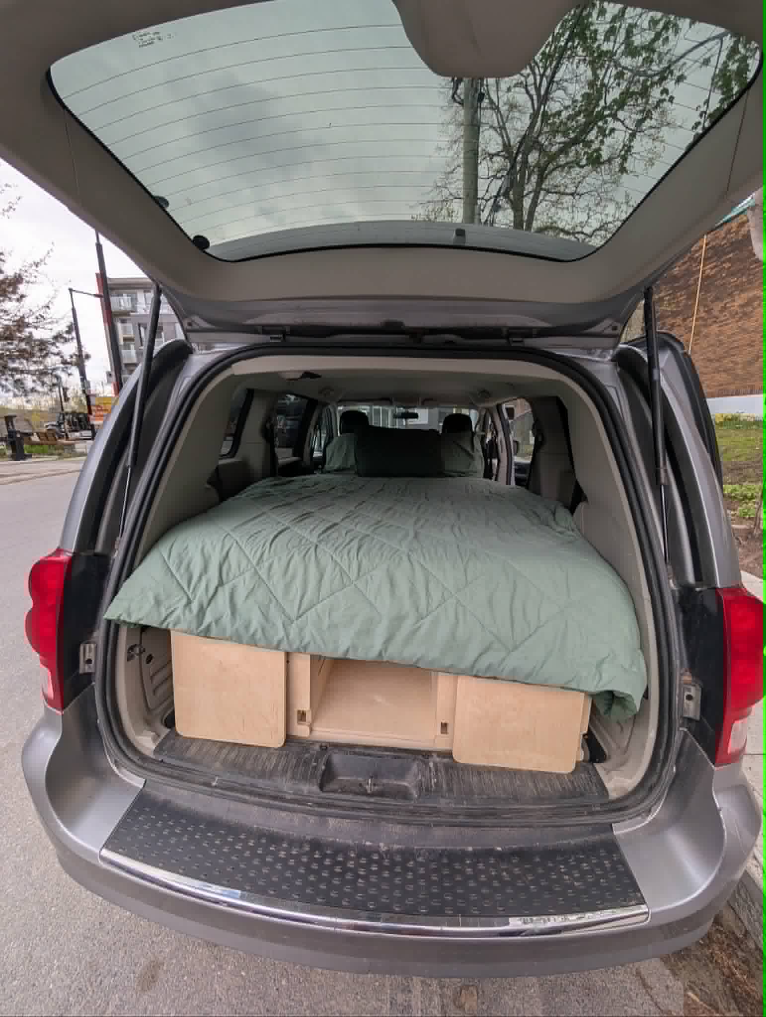 Inside this grey minivan, a comfy bed and storage boxes create a cozy camper conversion, ideal for an RV rental.. Dodge B Van 2014