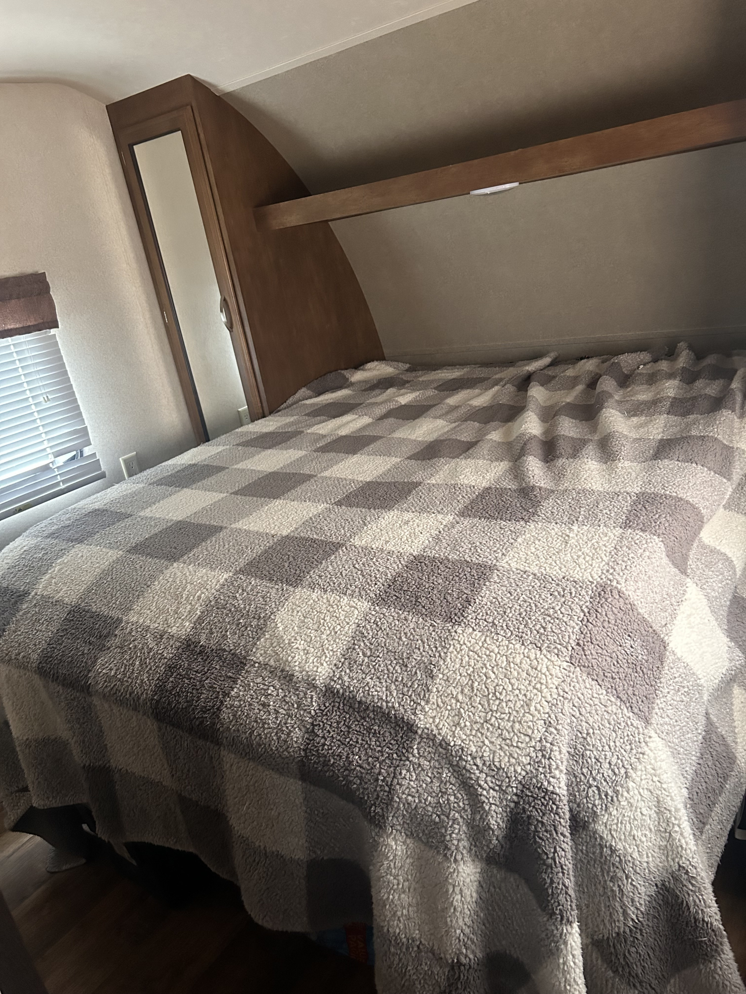 Cozy RV rental bedroom featuring a bed with a gray and white checkered sherpa blanket, window, and wooden cabinetry.. Forest River Wildwood 2017