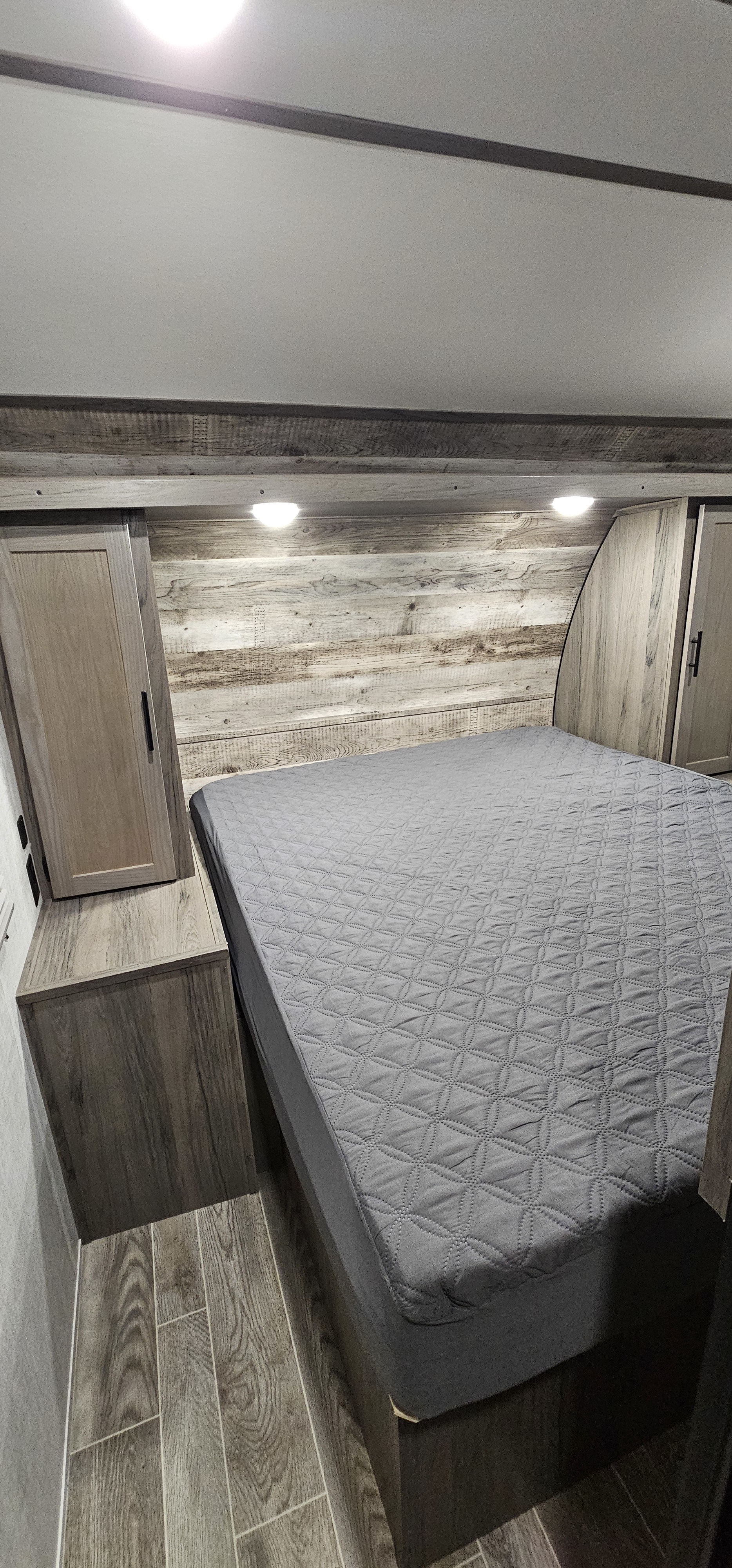 Cozy RV rental bedroom featuring a grey quilted bed, rustic wood paneling, and built-in storage cabinets.. Gulf Stream Grand River 29bhs 2022