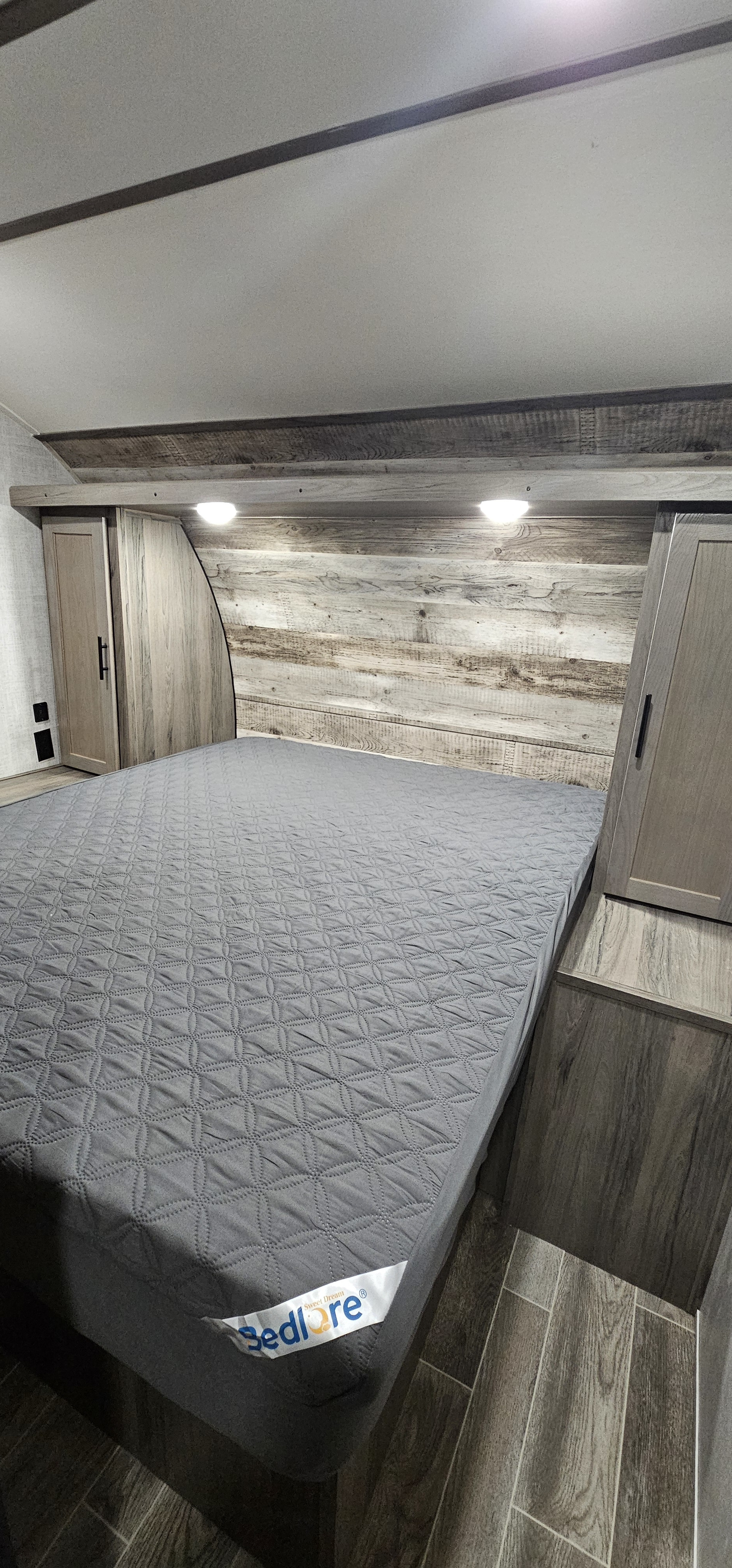 Cozy RV rental bedroom featuring a BedLóre mattress, rustic wood headboard, and compact storage cabinets.. Gulf Stream Grand River 29bhs 2022