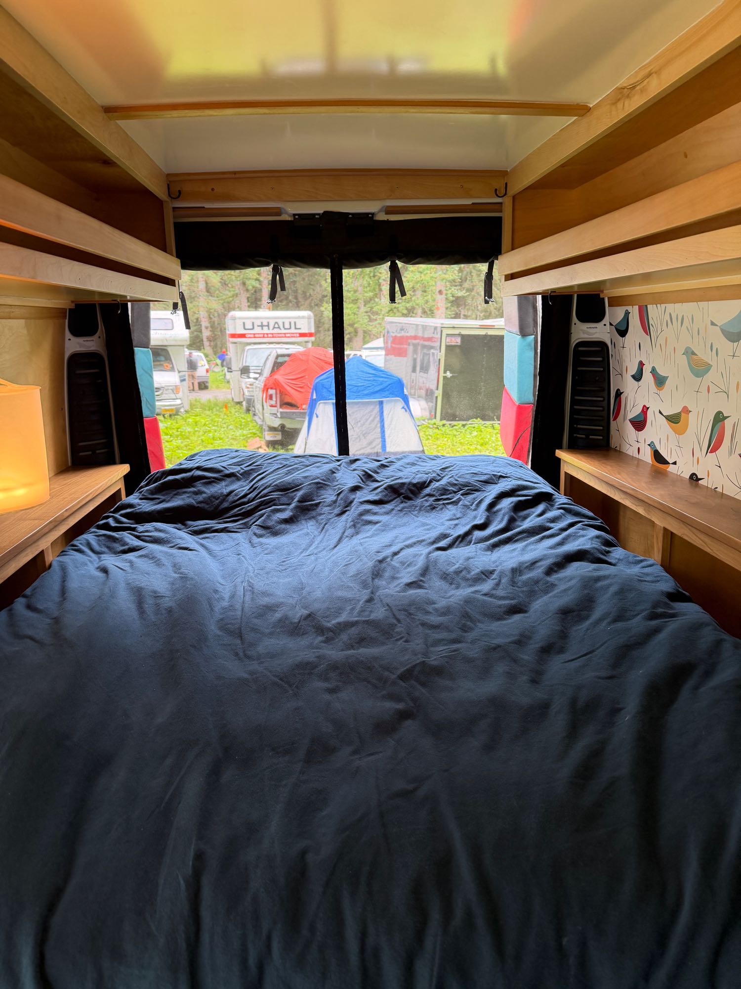 Cozy rv rental interior with a comfy bed, wooden shelves, and a view of other campers and tents outside.. 3C6TRVBGXHE551668 Ram Pro Master Van 2017