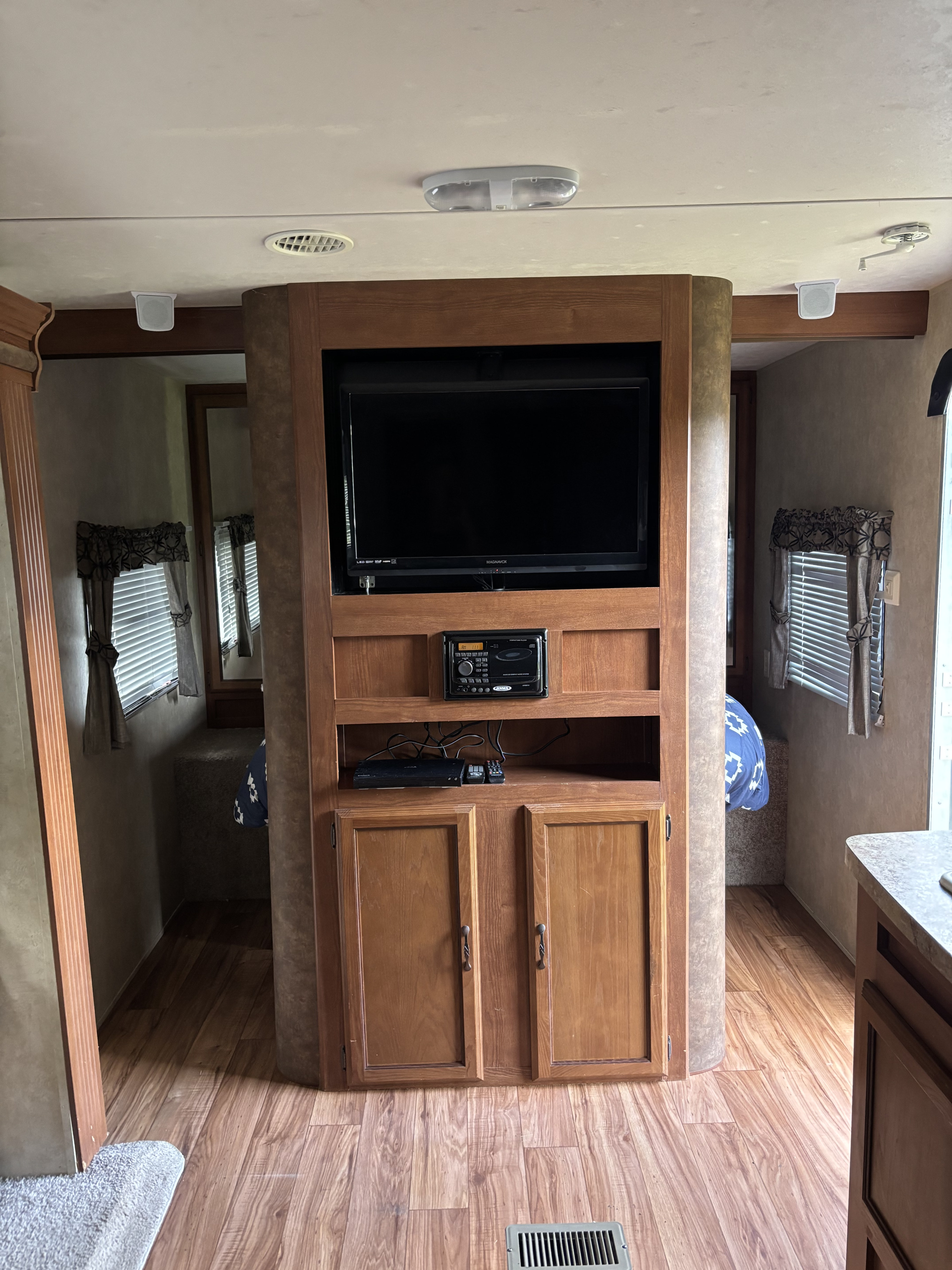 RV rental interior features a central entertainment center with TV & stereo, wood cabinetry, laminate flooring, and a glimpse of a bedroom.. Forest River Salem 2014