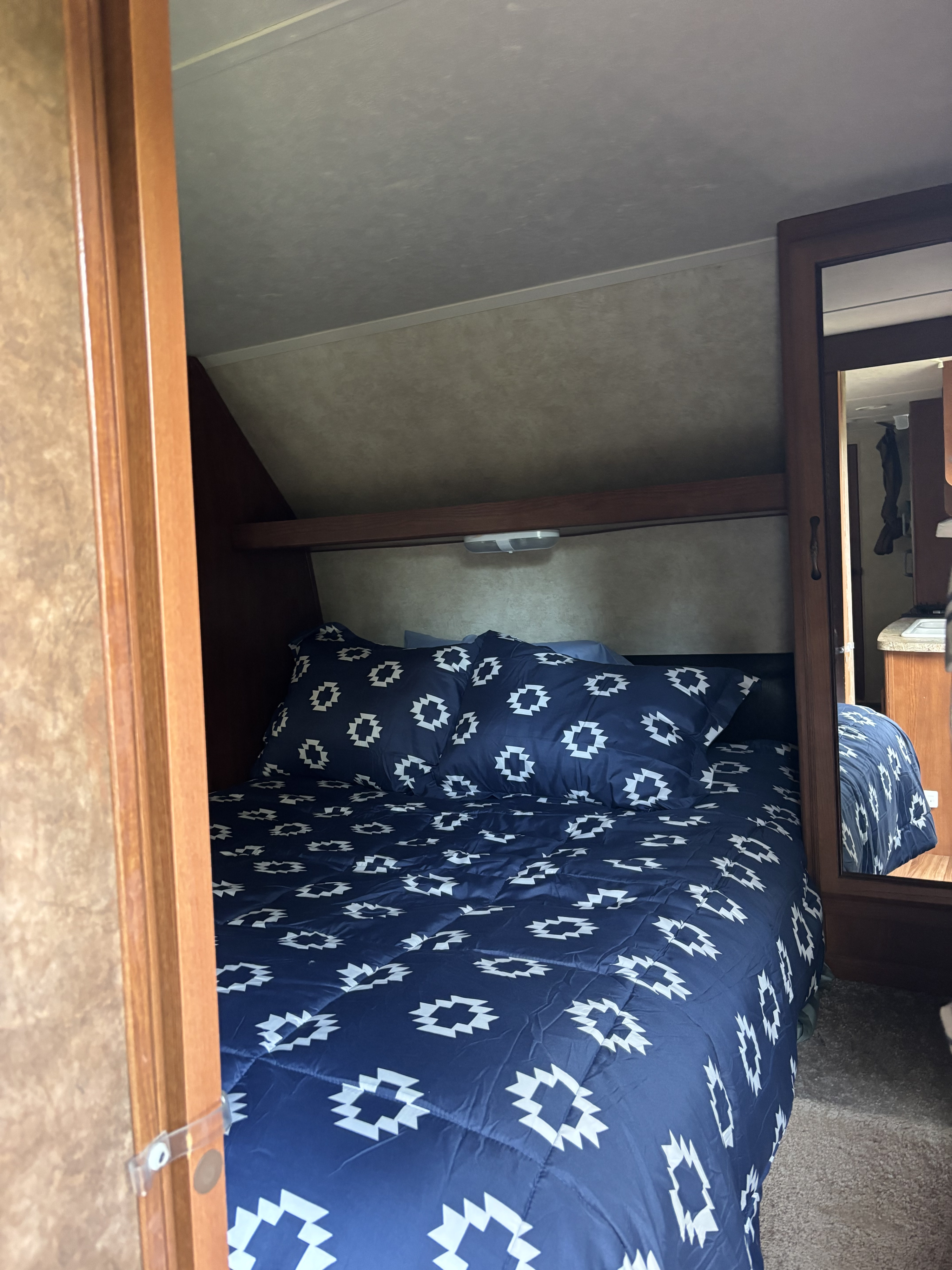 Cozy RV rental bedroom featuring a bed with blue and white patterned bedding, wood-paneled walls, and built-in storage.. Forest River Salem 2014