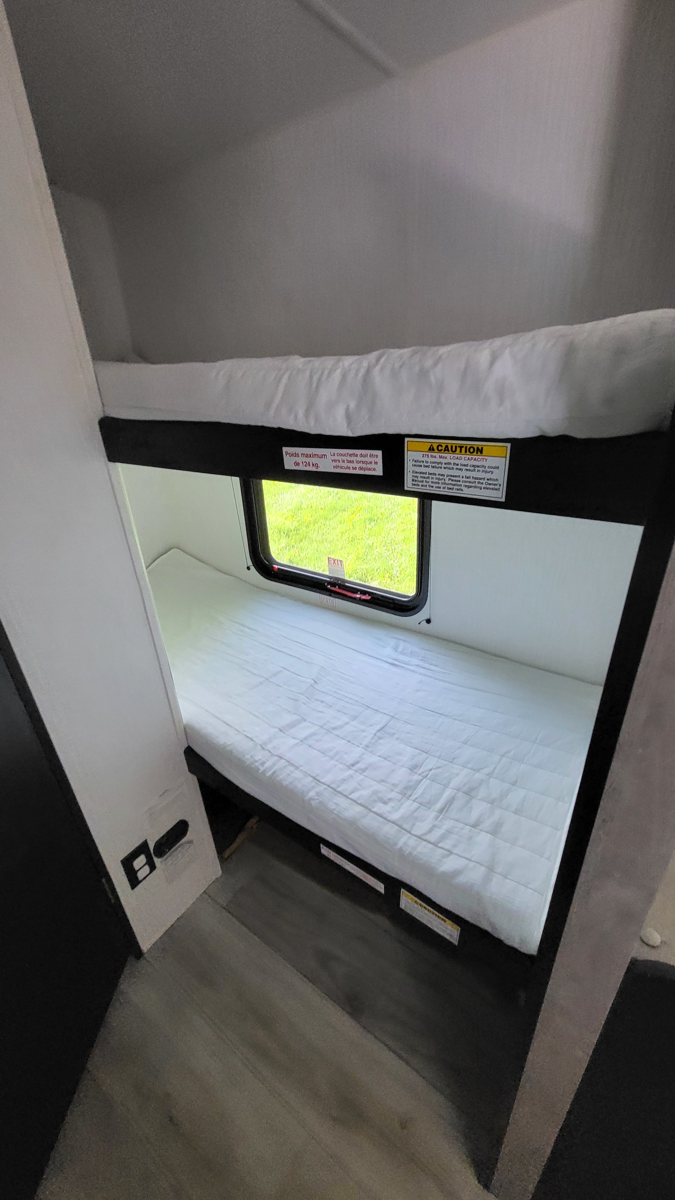 RV rental features comfortable bunk beds with a window overlooking green grass, ideal for family travel. Max load 275 lbs.. A Liner Ascape 2024