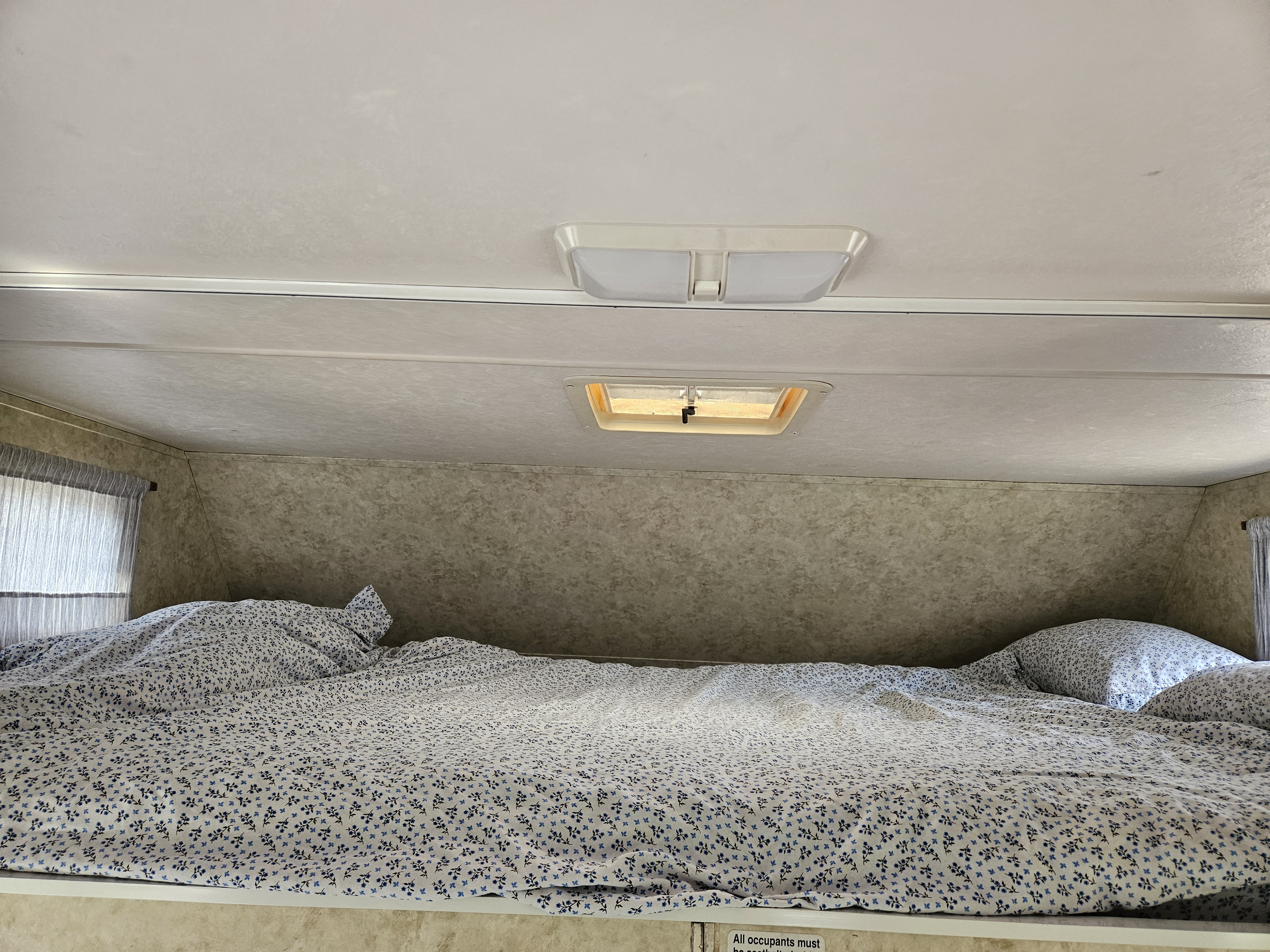Cozy RV rental bunk bed with floral bedding and overhead lights in a compact camper bedroom nook.. Ford Majestic 2004
