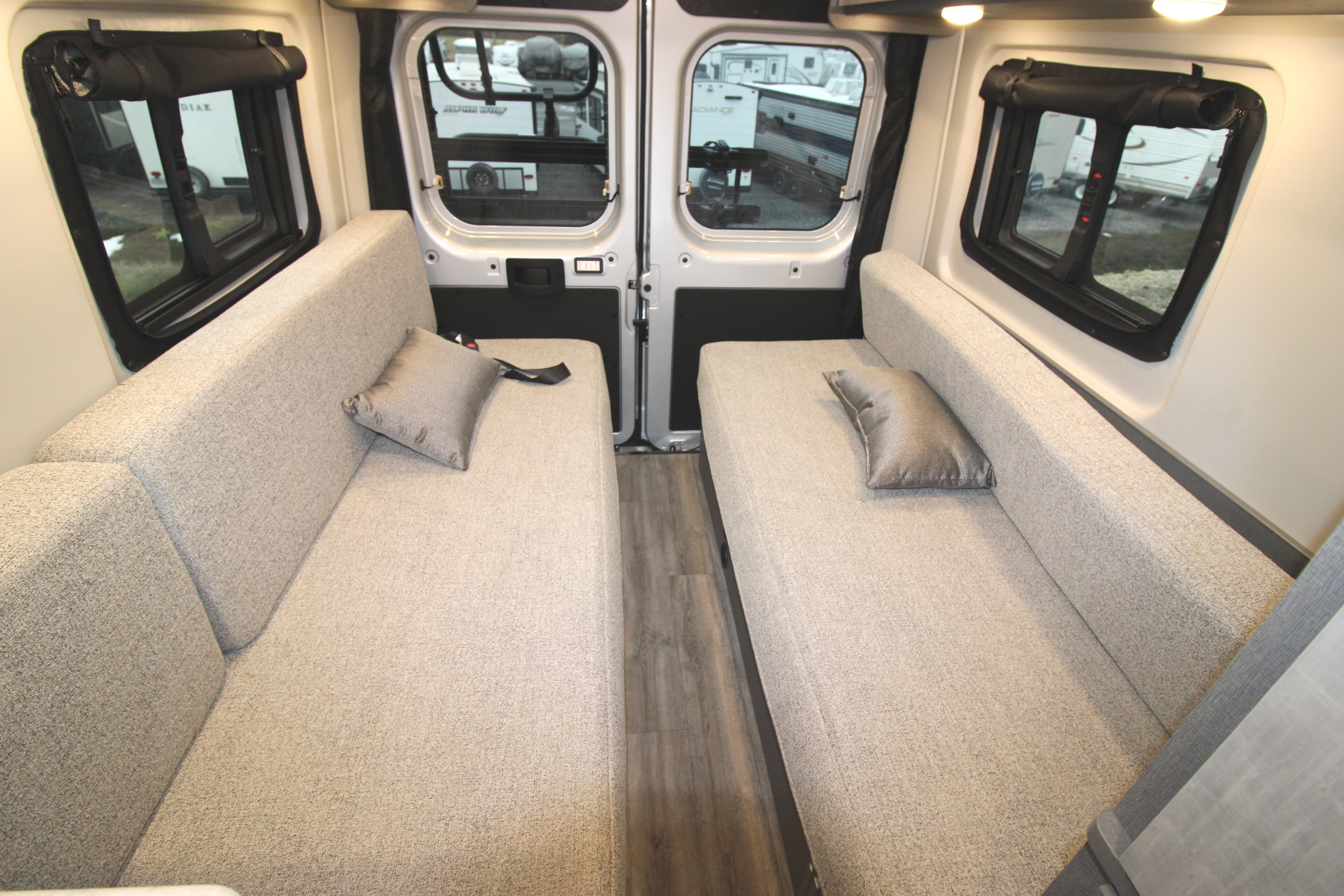 RV rental interior: two facing bench seats with cushions, convertible to beds, bordered by windows with shades & wood flooring.. Thor Motor Coach Tellaro 2026