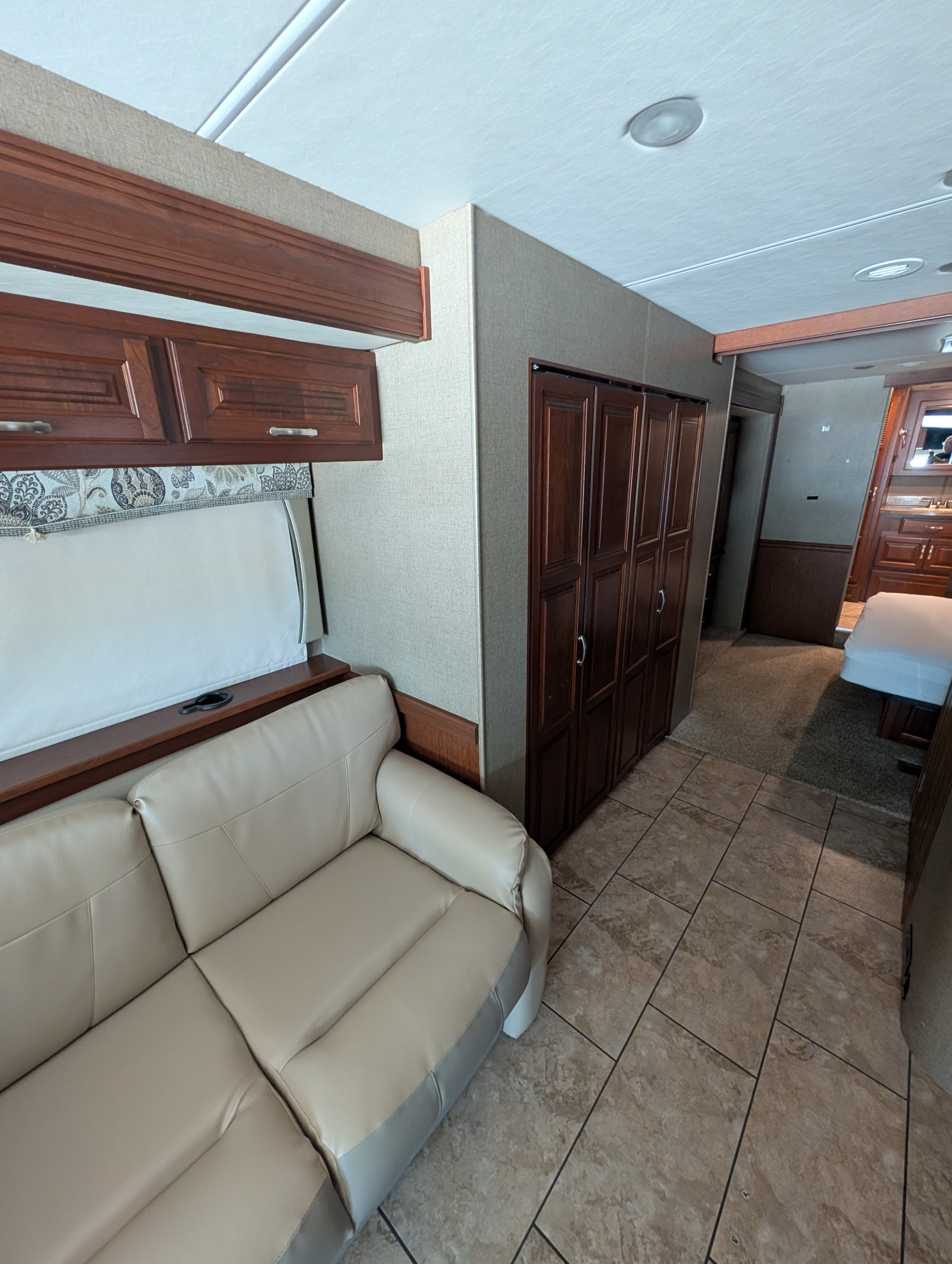 Clean rv rental interior. Features a beige sofa, dark wood cabinetry, patterned walls, and tiled flooring transitioning to carpet.. Forest River Berkshire 2018