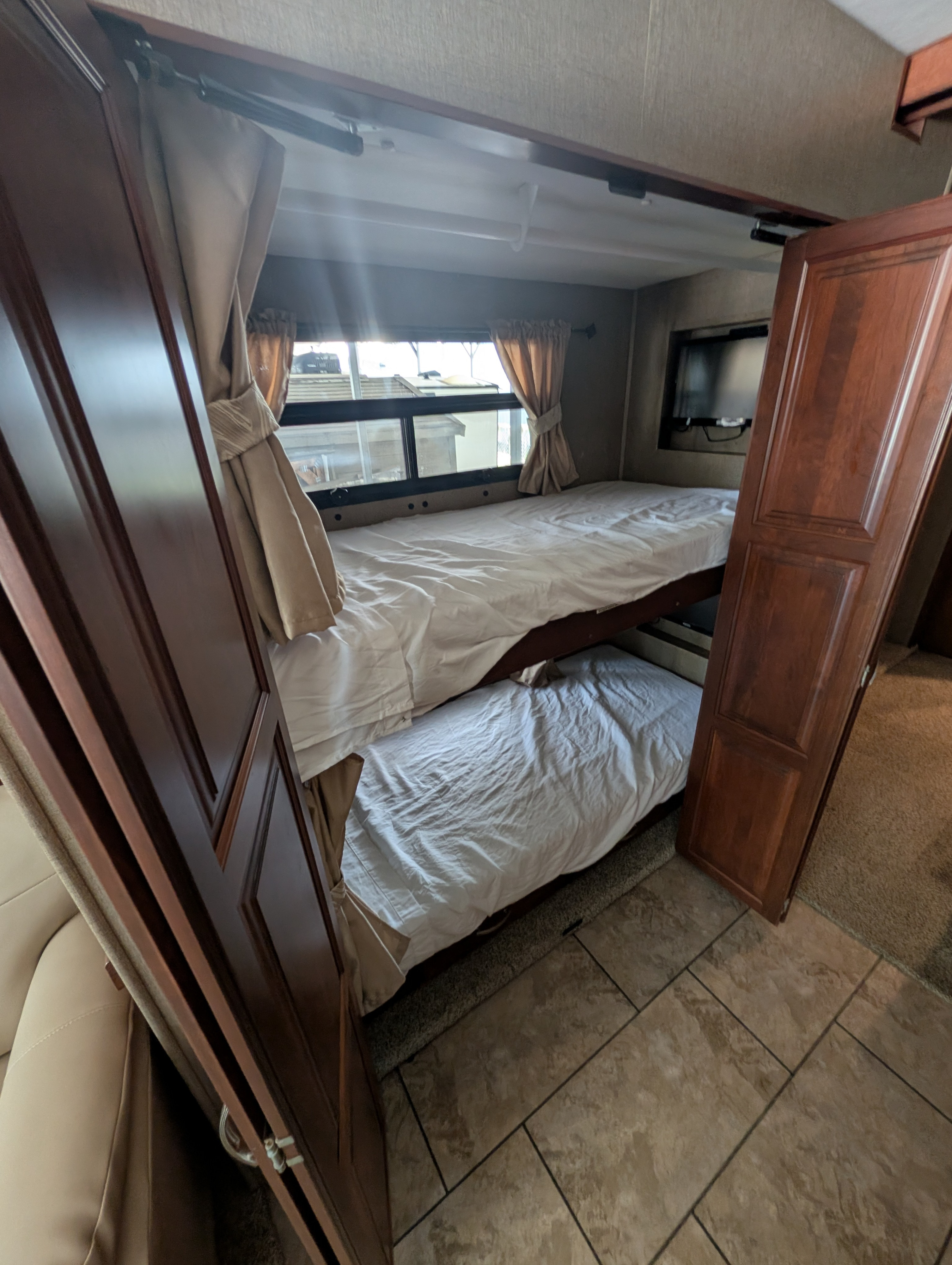 This RV rental bunk bed area shows two bunks with white bedding, window curtains, and a mounted TV for comfortable sleeping.. Forest River Berkshire 2018