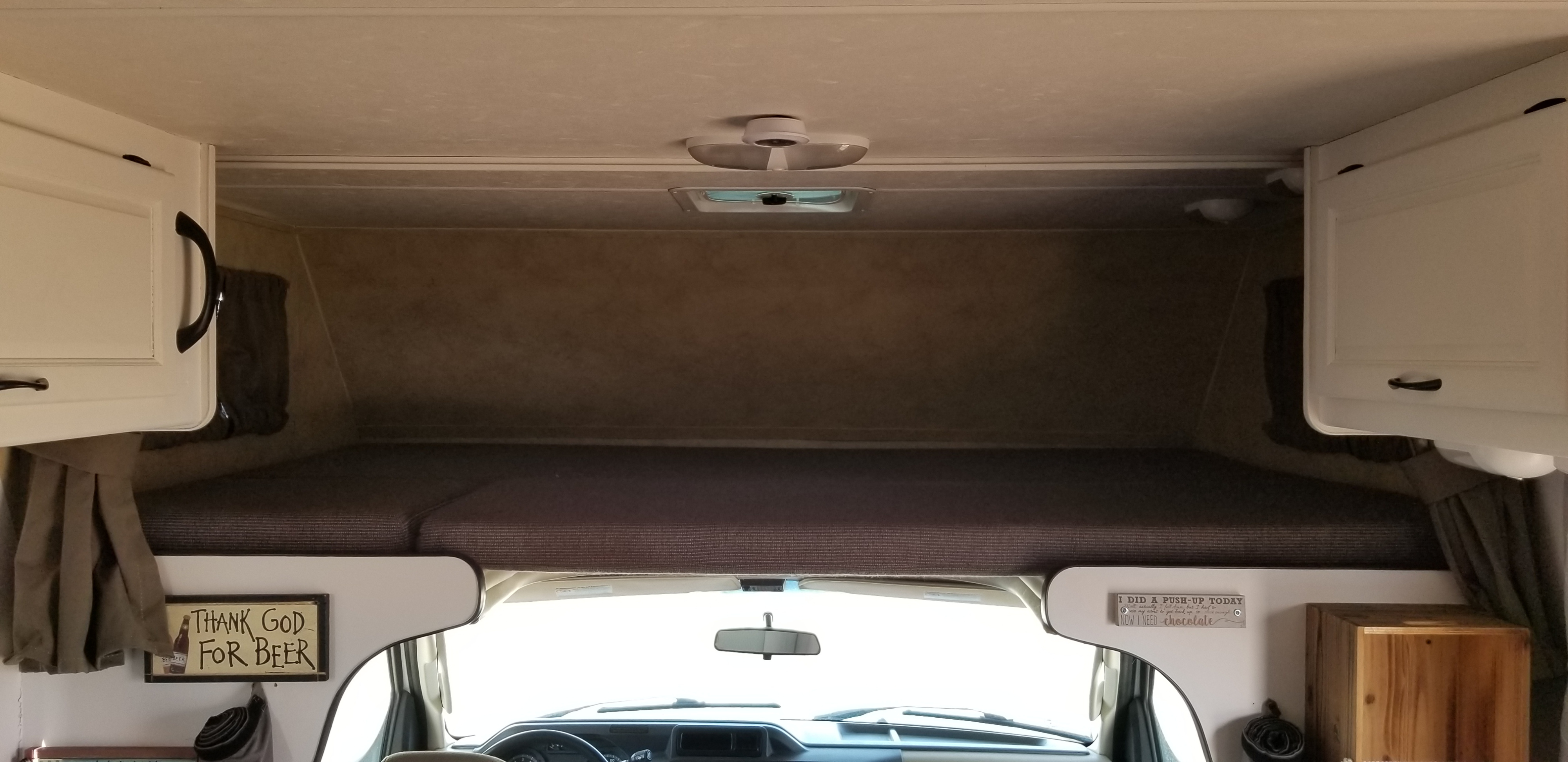 View from inside an RV rental looking towards the front. Overhead bunk, driver's cabin, white cabinets, & humorous signs.. Thor Majestic 2013