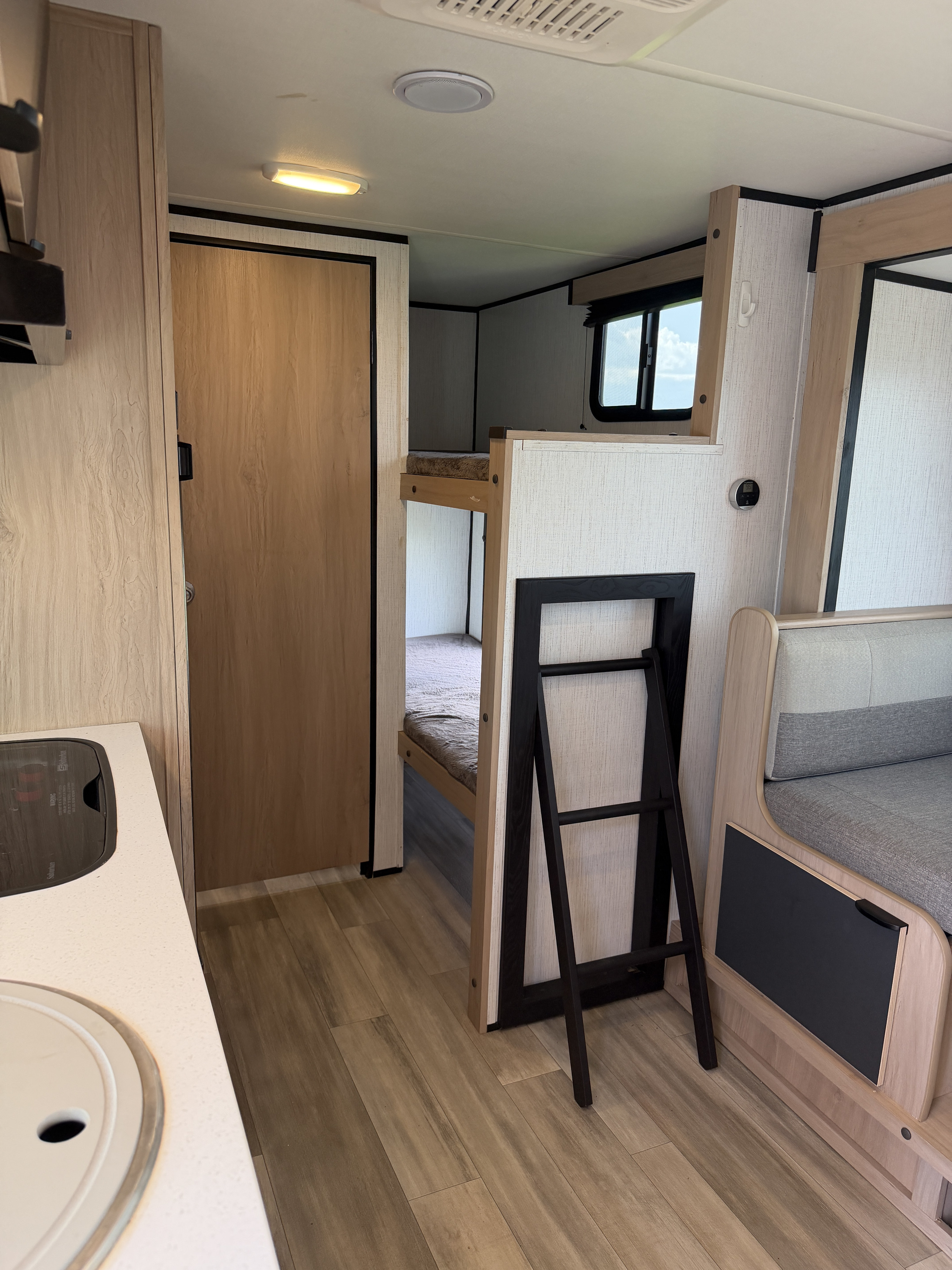 Inside this modern rv rental: a light-toned kitchen counter, a closed door, cozy bunk beds with a ladder, and dinette seating.. Cruiser RV Hitch 2022