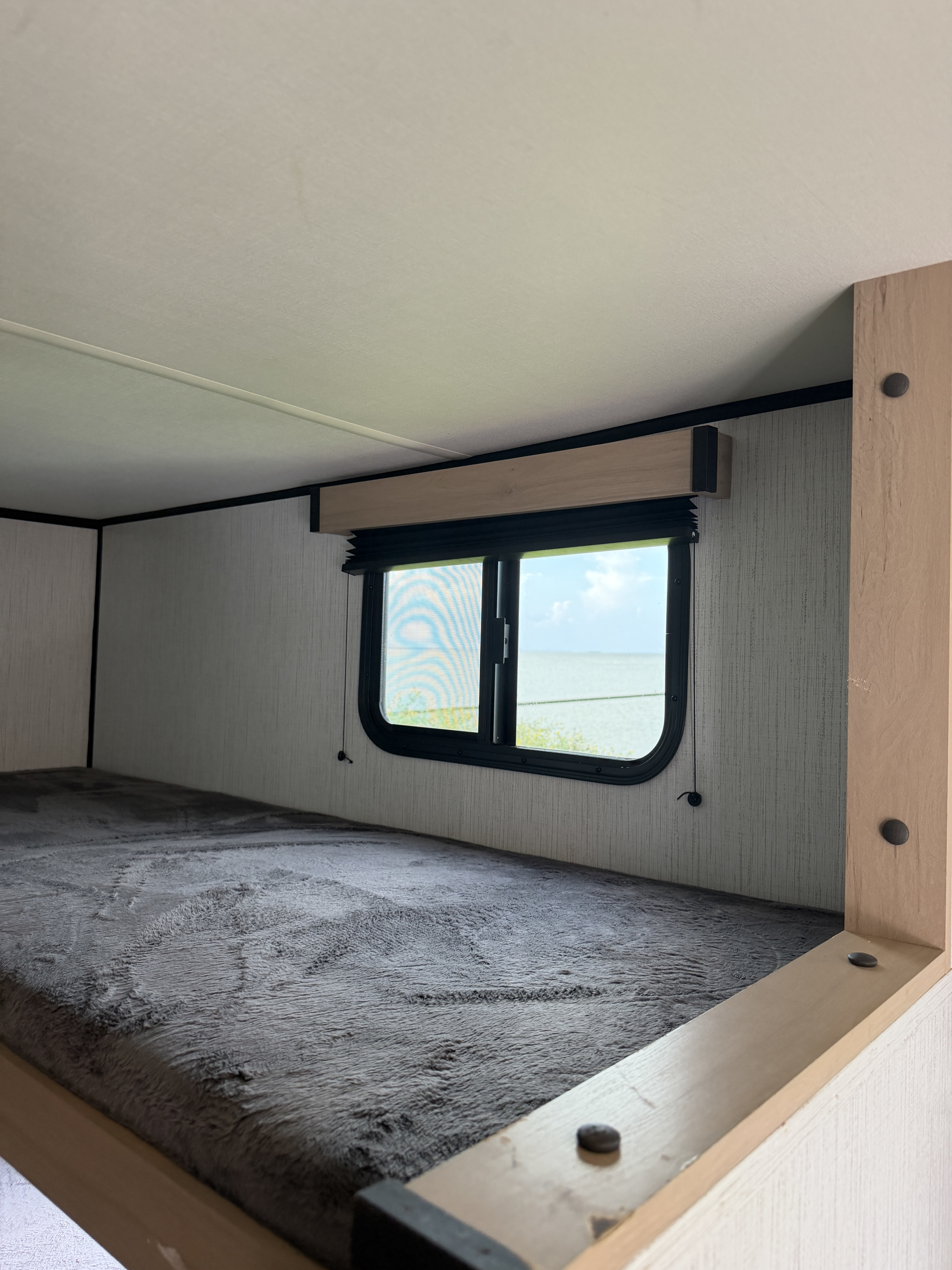 Cozy RV rental bunk bed interior with a fluffy grey blanket and a window offering serene water views.. Cruiser RV Hitch 2022