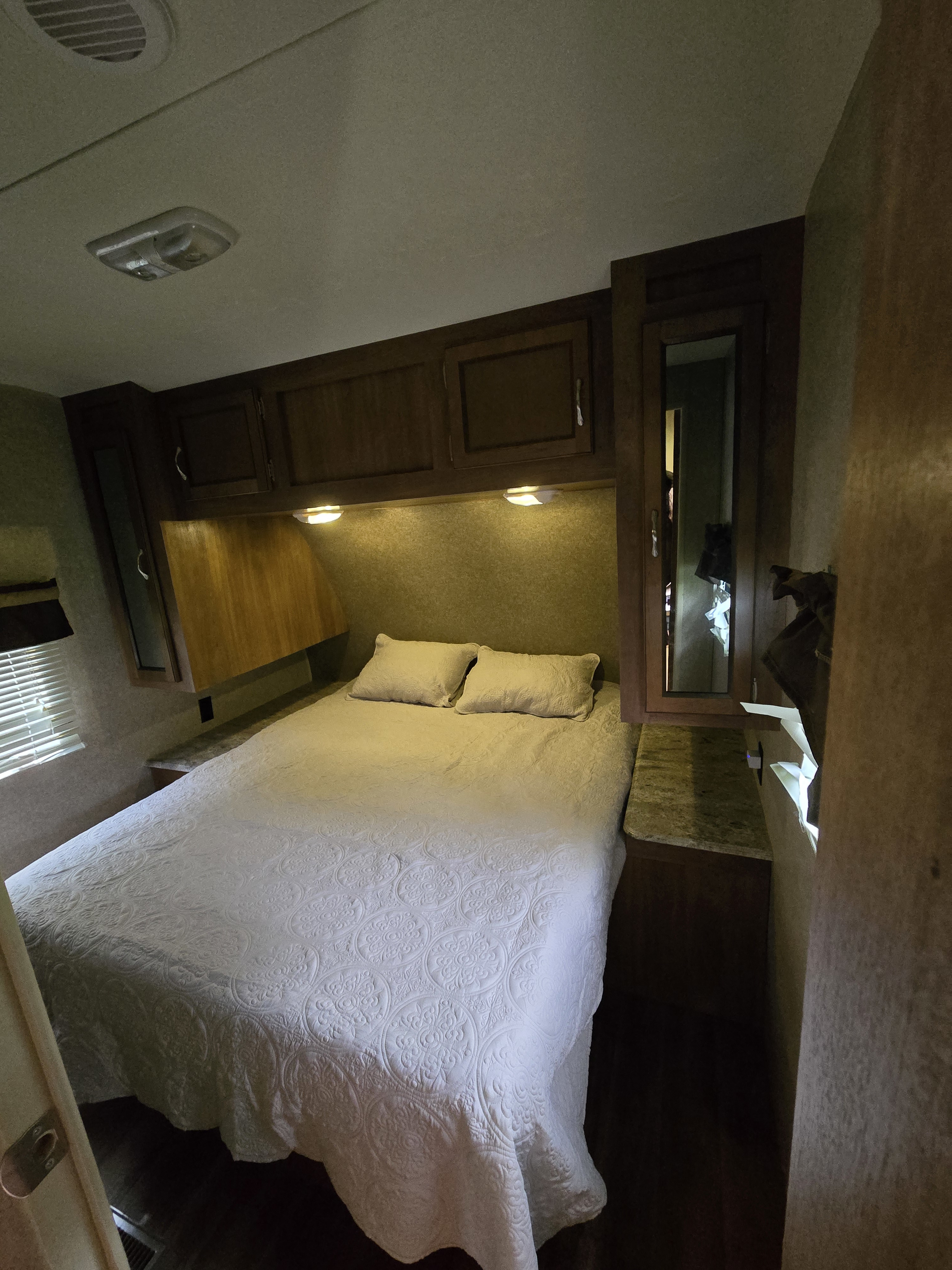 Cozy RV rental bedroom with a quilted bed, overhead cabinets, and reading lights. Compact and functional travel trailer interior.. Coachmen Catalina 2017