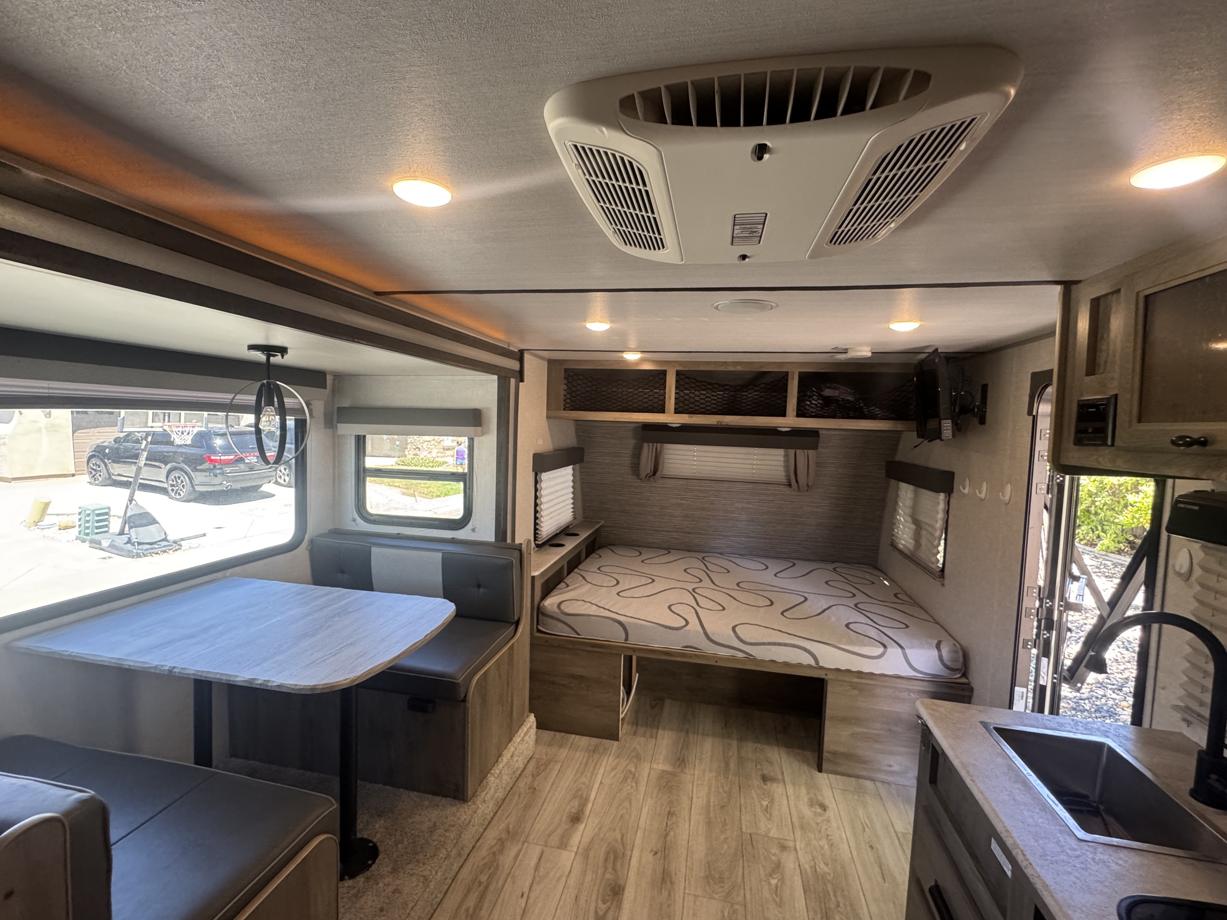 Interior of an RV rental: dinette with grey benches, patterned bed, kitchen sink, and overhead AC unit. Bright and functional space.. Forest River Surveyor Legend 2023