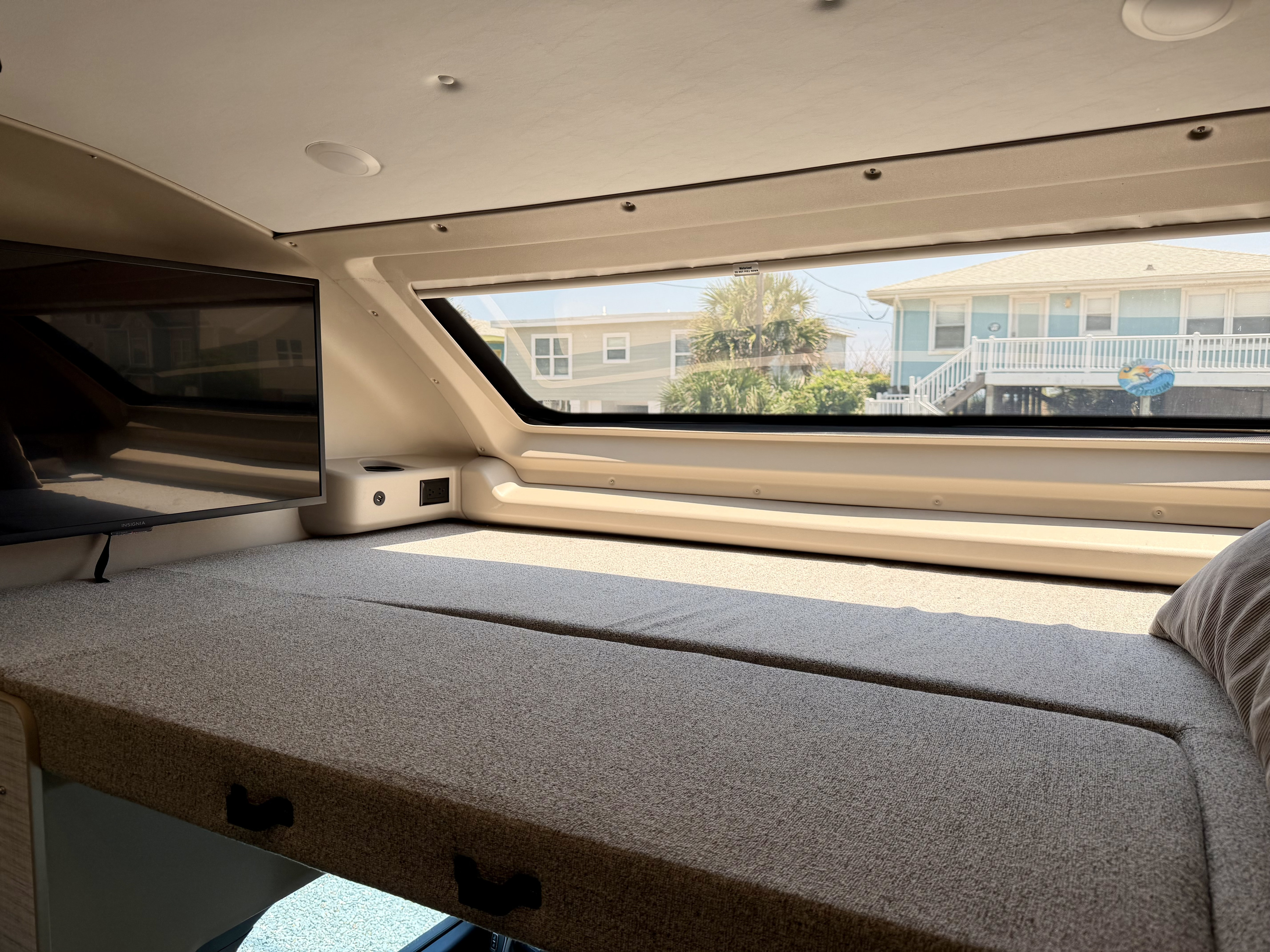 Inside this RV rental, find a comfy bed, TV, and a large window showcasing coastal homes. Ideal for vacationing.. Entegra Coach Esteem XL 2024