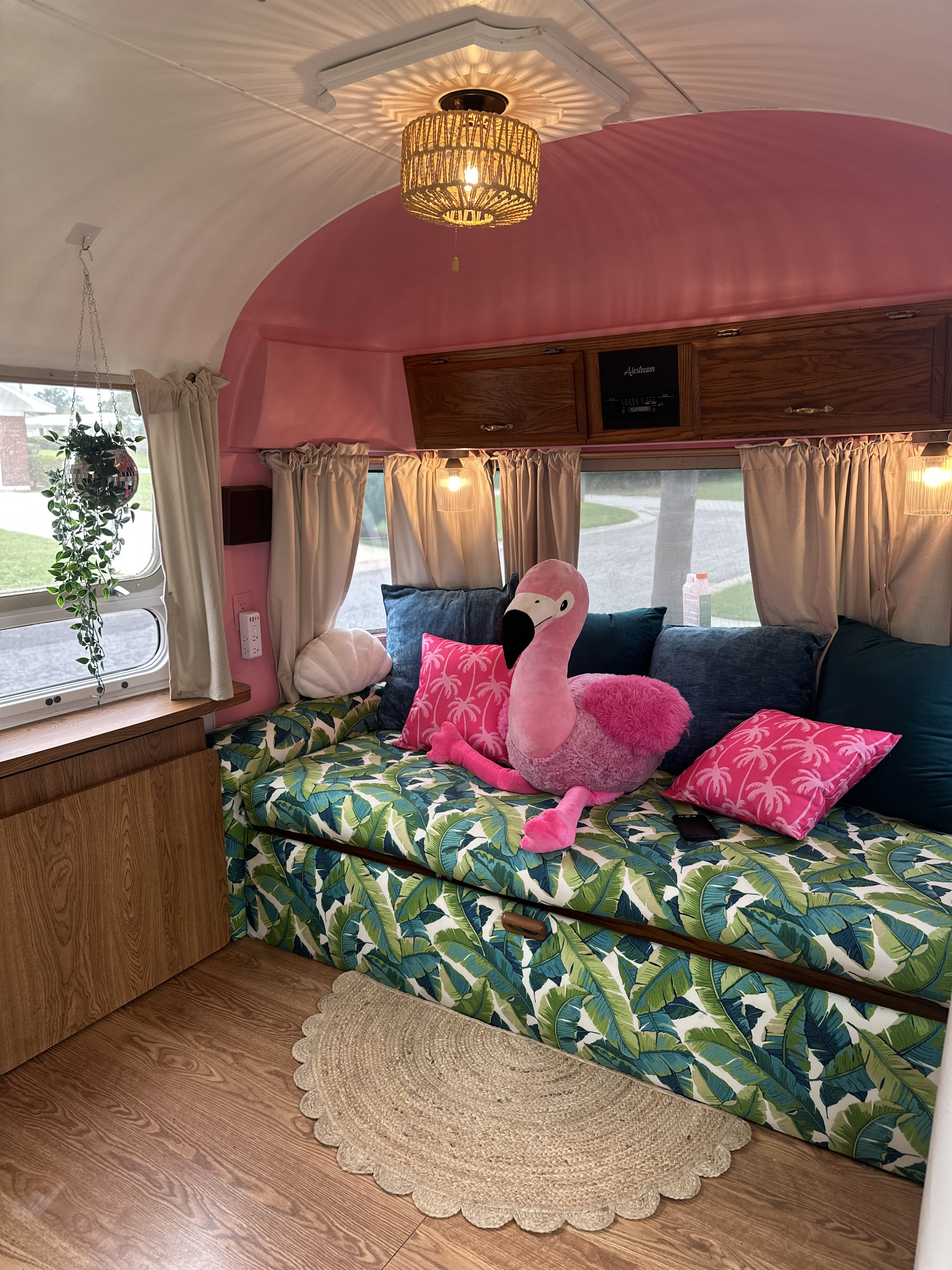 This vibrant RV rental features a pink and tropical-themed interior with a banana leaf couch, flamingo plush, and disco ball planter.. Airstream Excella 1991