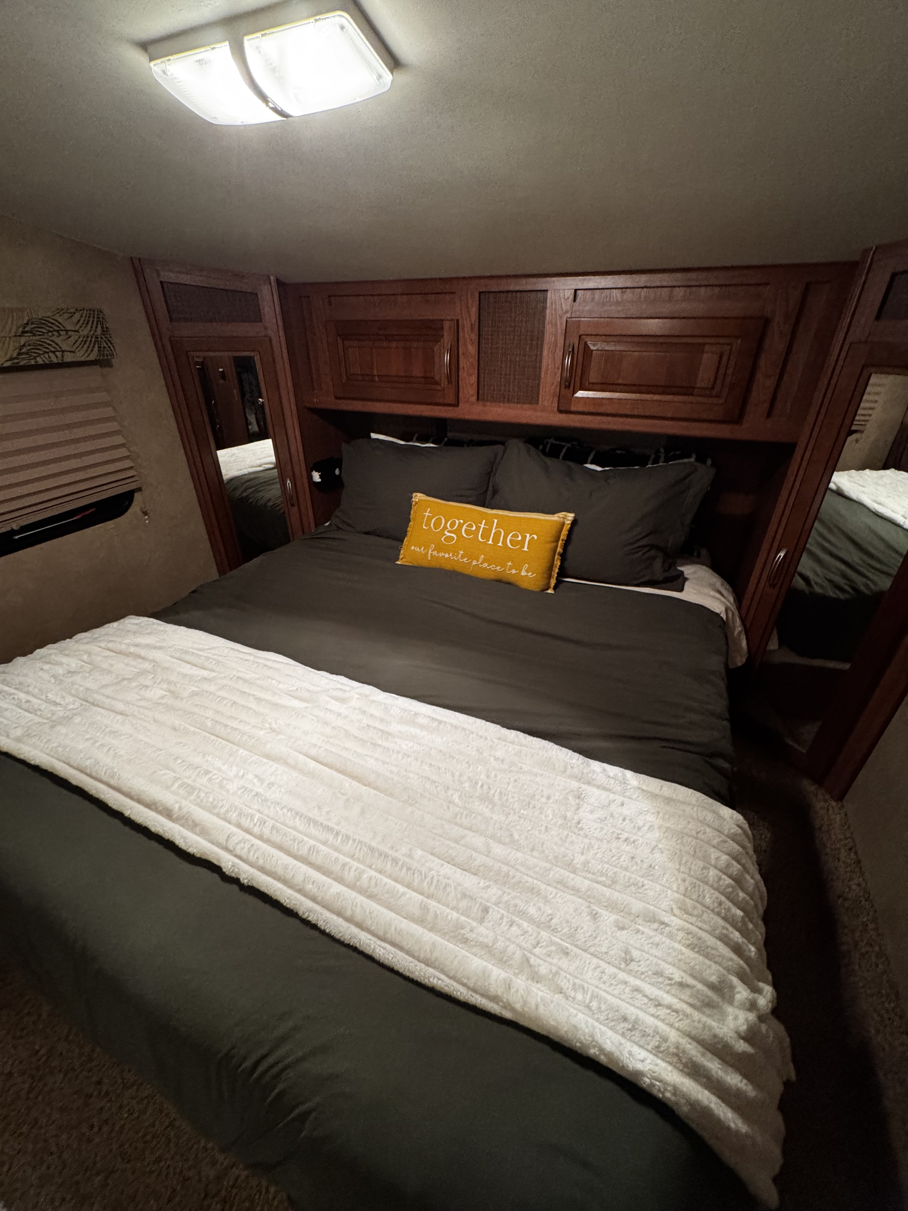 Cozy RV rental bedroom: dark bedding, "together" pillow, soft white throw, wood cabinetry, and overhead lighting.. Forest River Wildcat Extralite 2012
