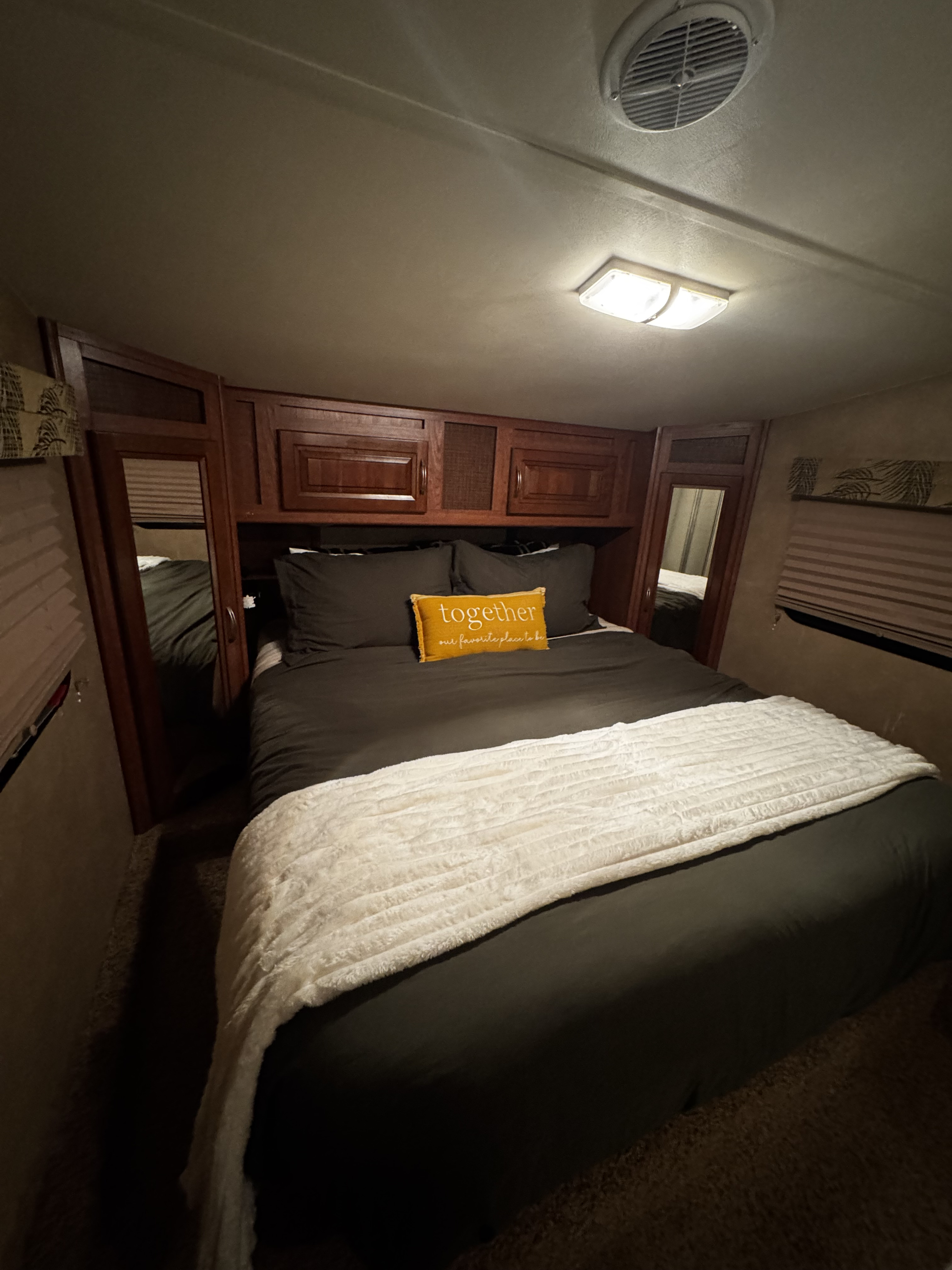 Inviting rv rental bedroom showcasing a bed with dark bedding, a "together" pillow, white blanket, & wood overhead storage.. Forest River Wildcat Extralite 2012