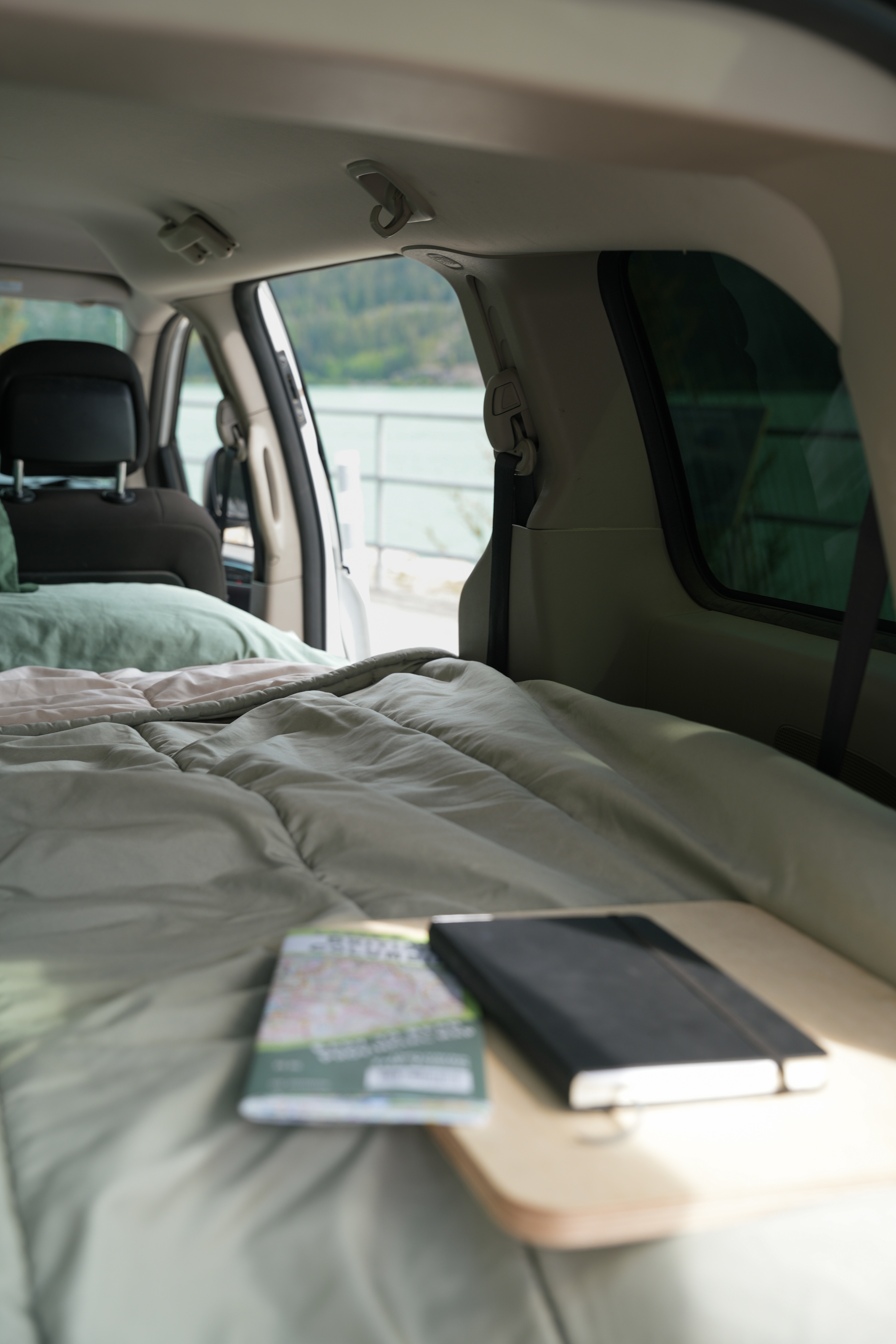 Cozy bed in an RV rental, with a map & notebook, overlooking a scenic lake. Perfect for van life adventures.. Dodge B Van 2017