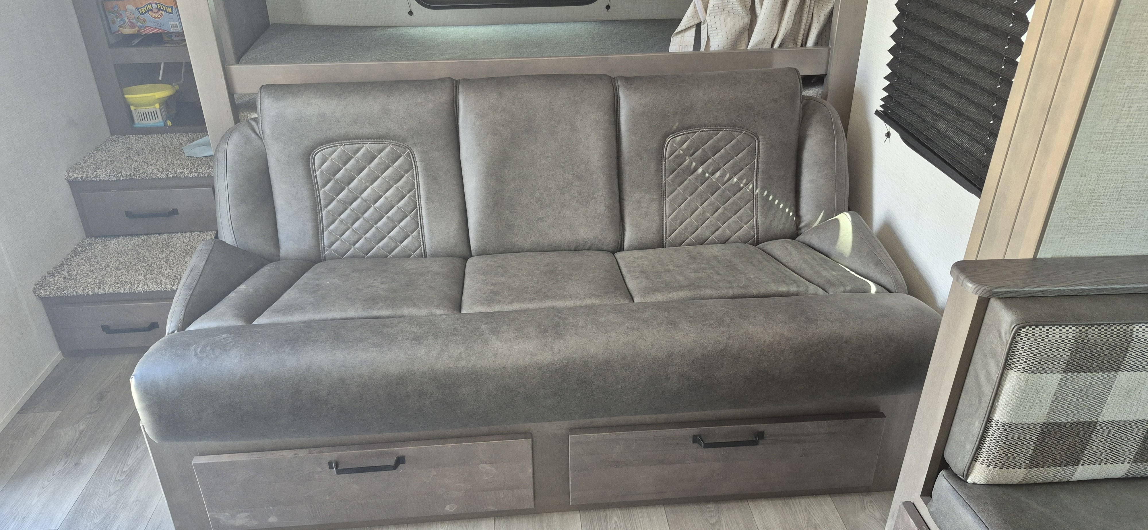 Cozy RV rental interior featuring a grey sofa with quilted backrests, storage drawers, and a bunk area.. Grand Design Transcend Xplor 2024