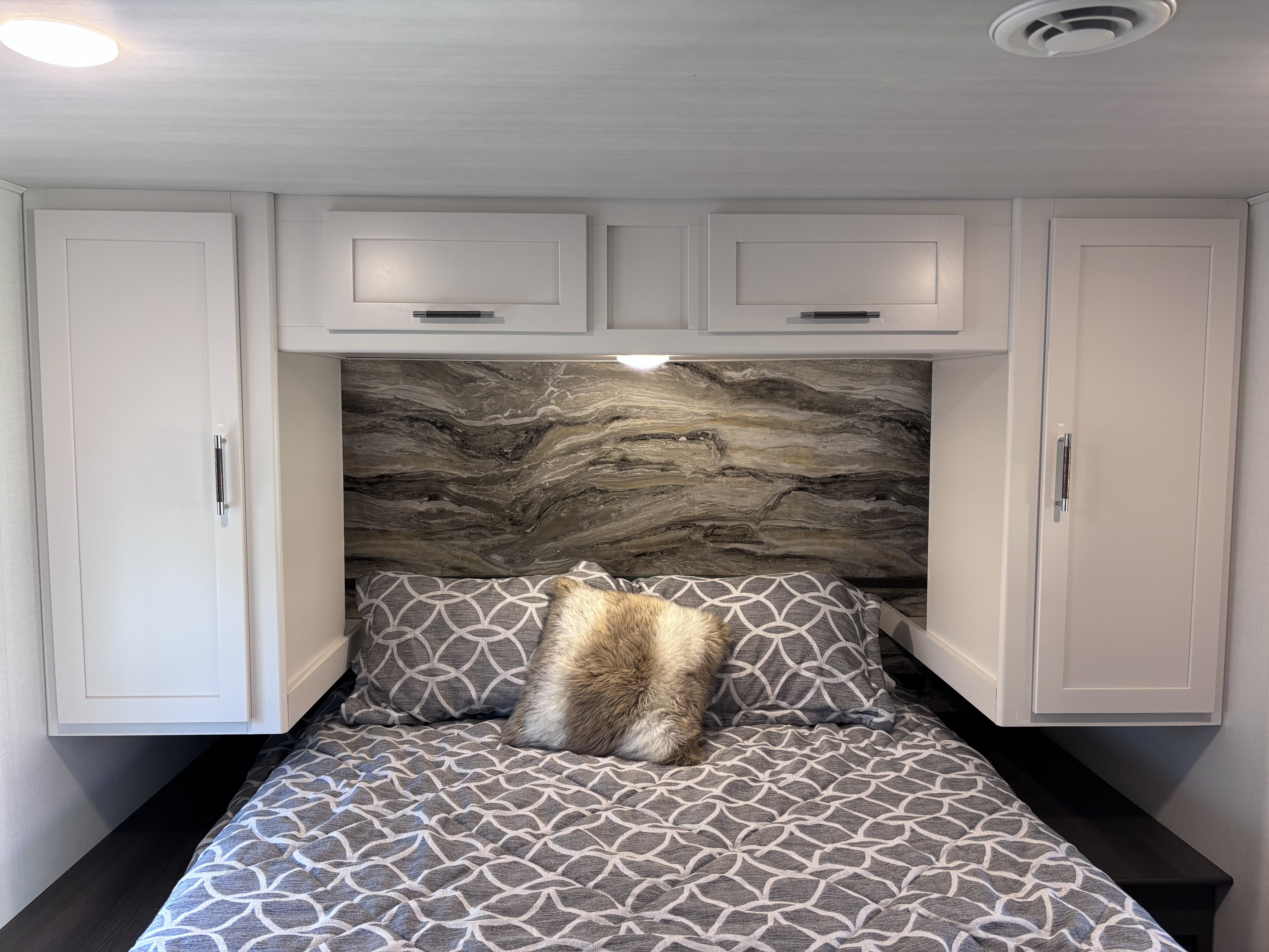 Cozy RV rental bedroom featuring modern white cabinets, a striking marbled backsplash, and a comfy bed with patterned linens.. Keystone RV Bullet Classic 2025
