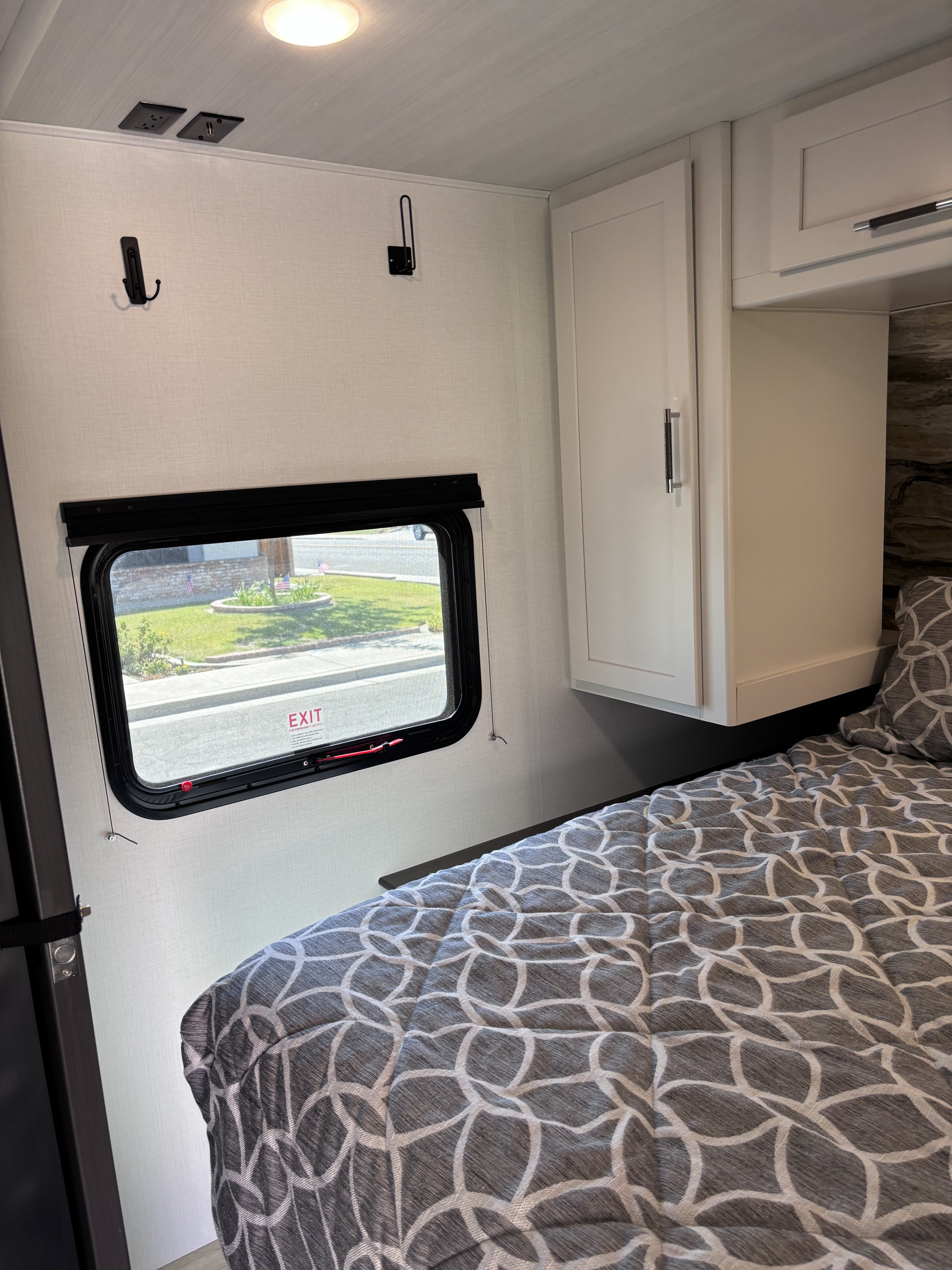 Cozy rv rental bedroom with a geometric patterned comforter, window, overhead cabinets, wall hooks, and power outlets.. Keystone RV Bullet Classic 2025