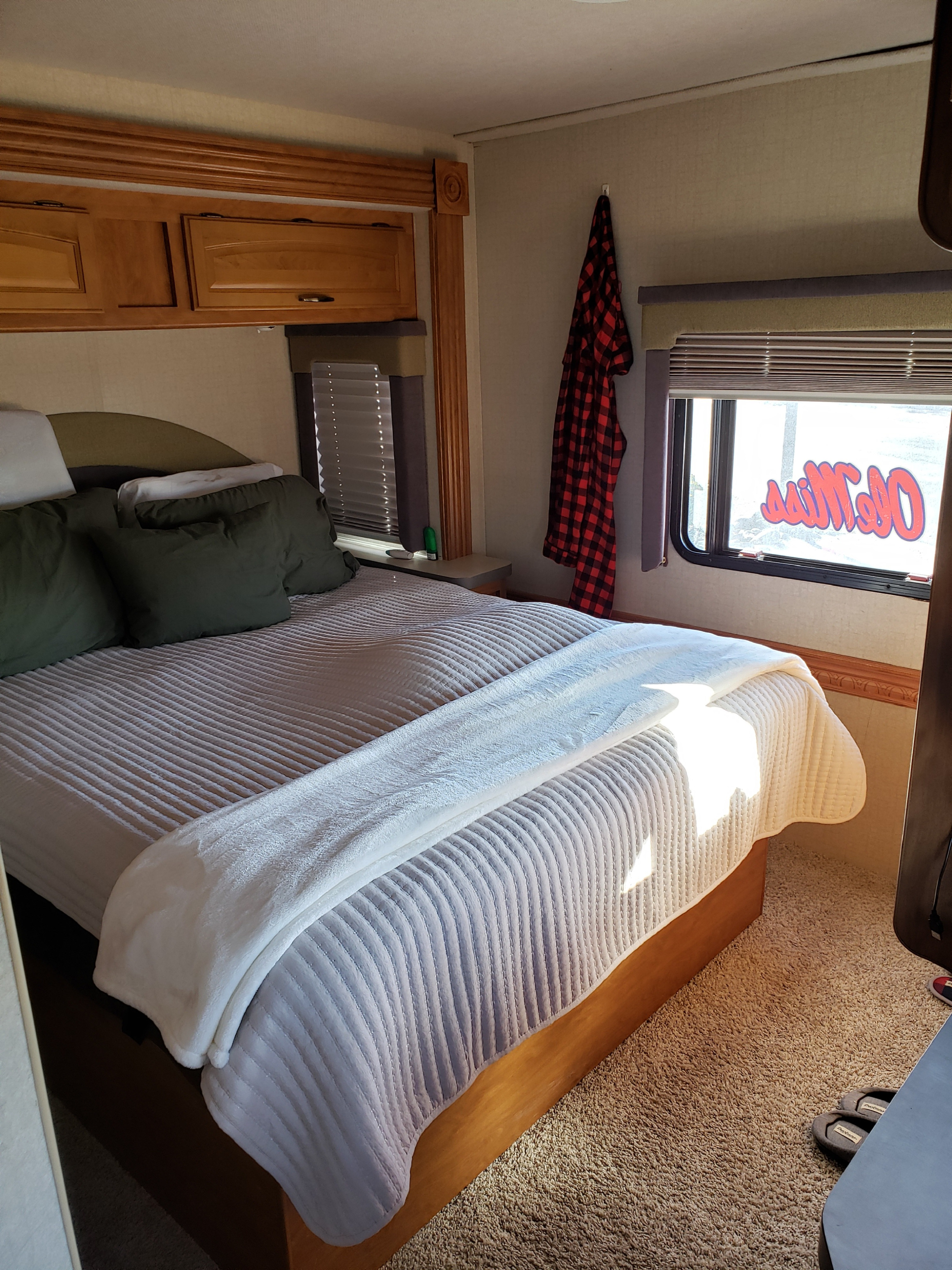Inside an RV rental bedroom: A comfortable bed with green and white pillows, white blankets, wood cabinetry, and a window.. Fleetwood Tioga 31M 2007