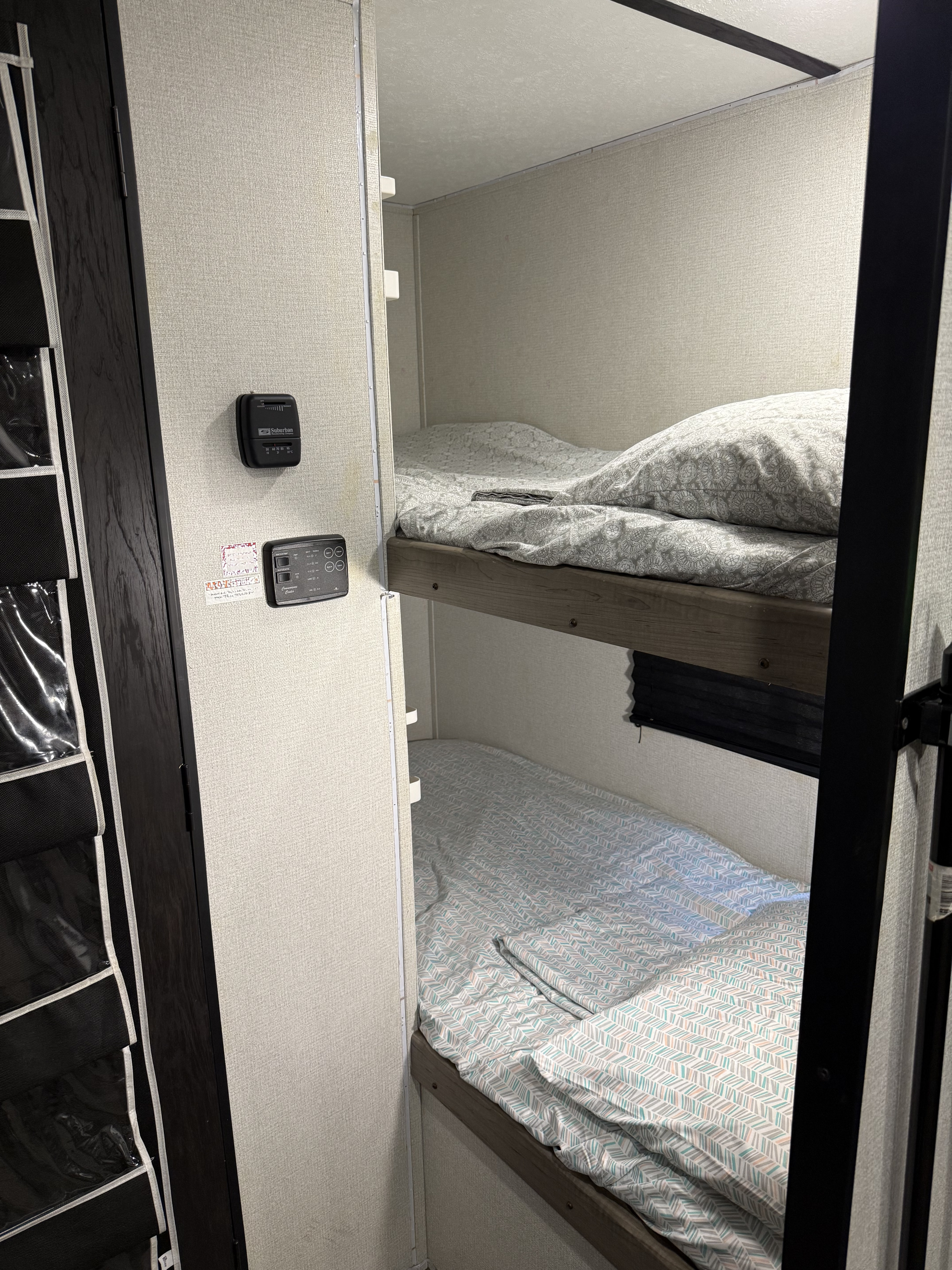 RV rental interior: Two cozy bunk beds with patterned bedding, a wall-mounted thermostat, and system controls.. Keystone RV Hideout 2021