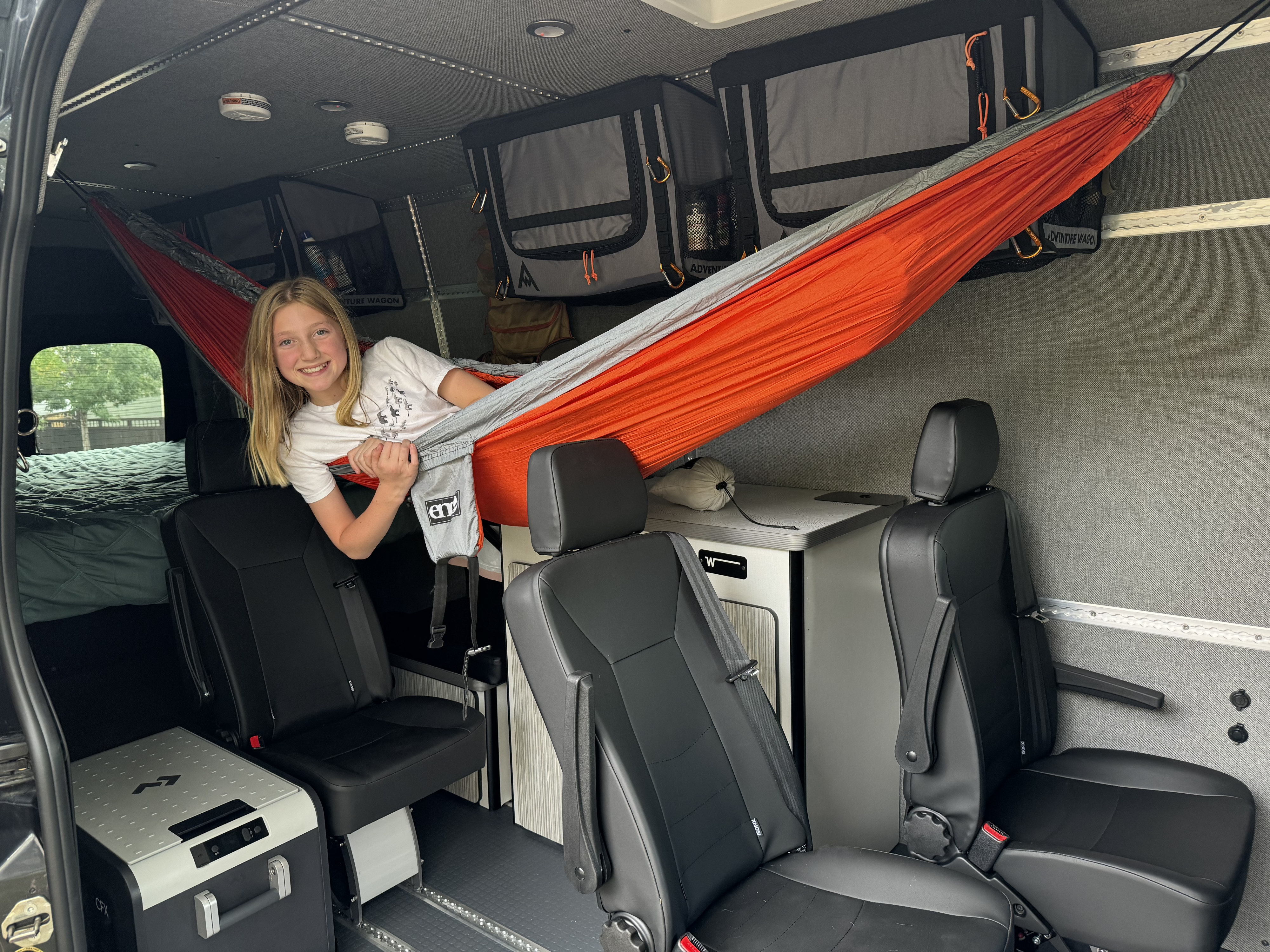 Smiling girl relaxes in a hammock inside this custom rv rental van, showcasing its family-friendly setup for adventure.. Winnebago Adventure Wagon 2023
