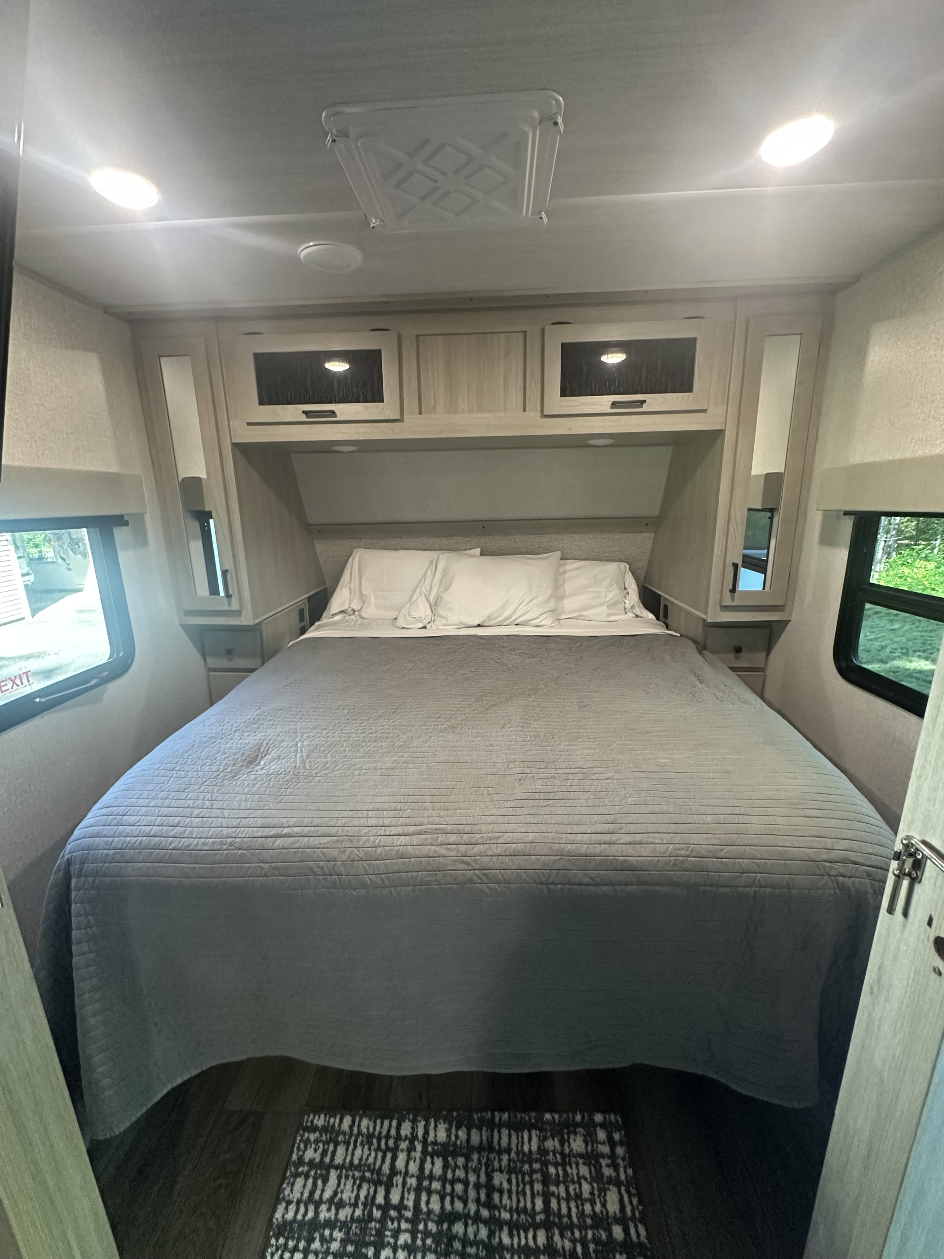Cozy RV rental bedroom featuring a comfy bed, overhead storage, side mirrors, and windows for natural light.. East to West Alta 2022