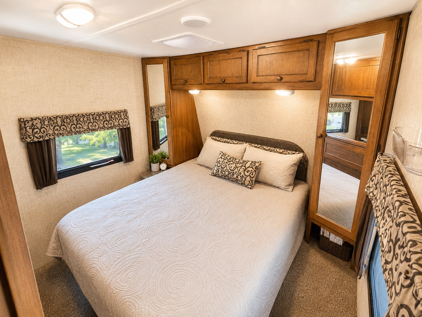 Comfortable RV rental bedroom featuring a queen bed, quilted coverlet, window view, wood cabinets, and mirrored wardrobe.. Keystone Sprinter 2014