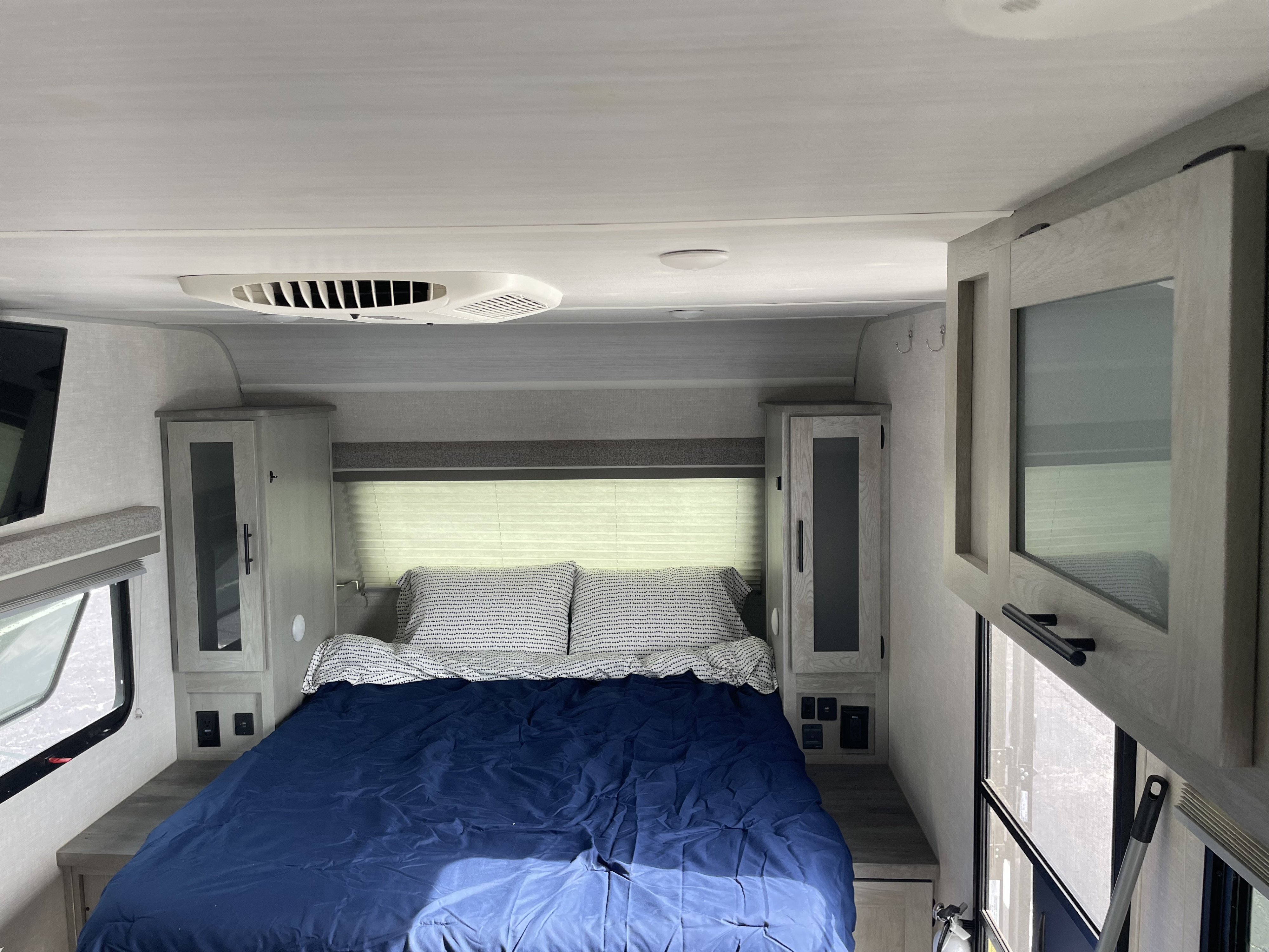 Bright RV rental bedroom with a blue bed, surrounding storage, and an AC unit, providing comfort in a compact space.. Forest River Ibex 2022