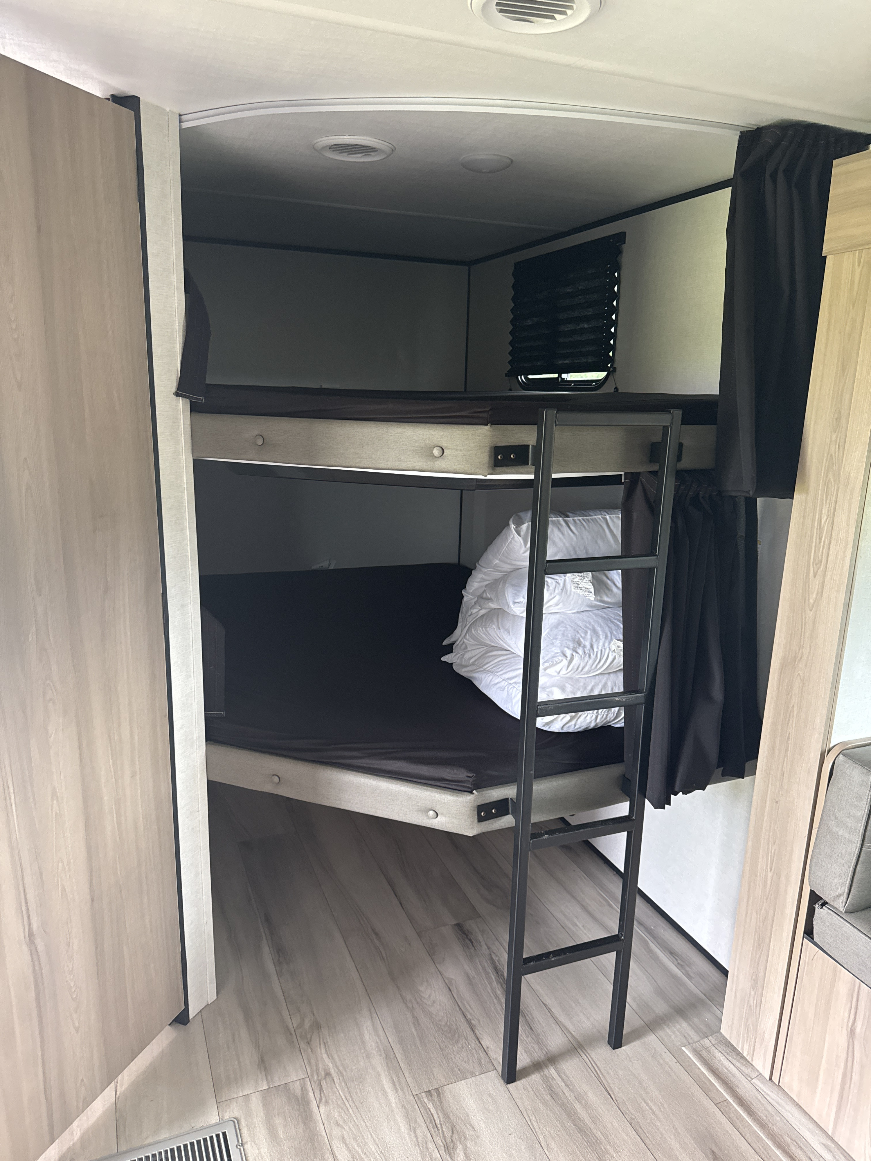 RV rental with cozy bunk beds. Features a metal ladder, dark mattresses, and curtains for privacy in a compact space.. Keystone RV Coleman Light 2026