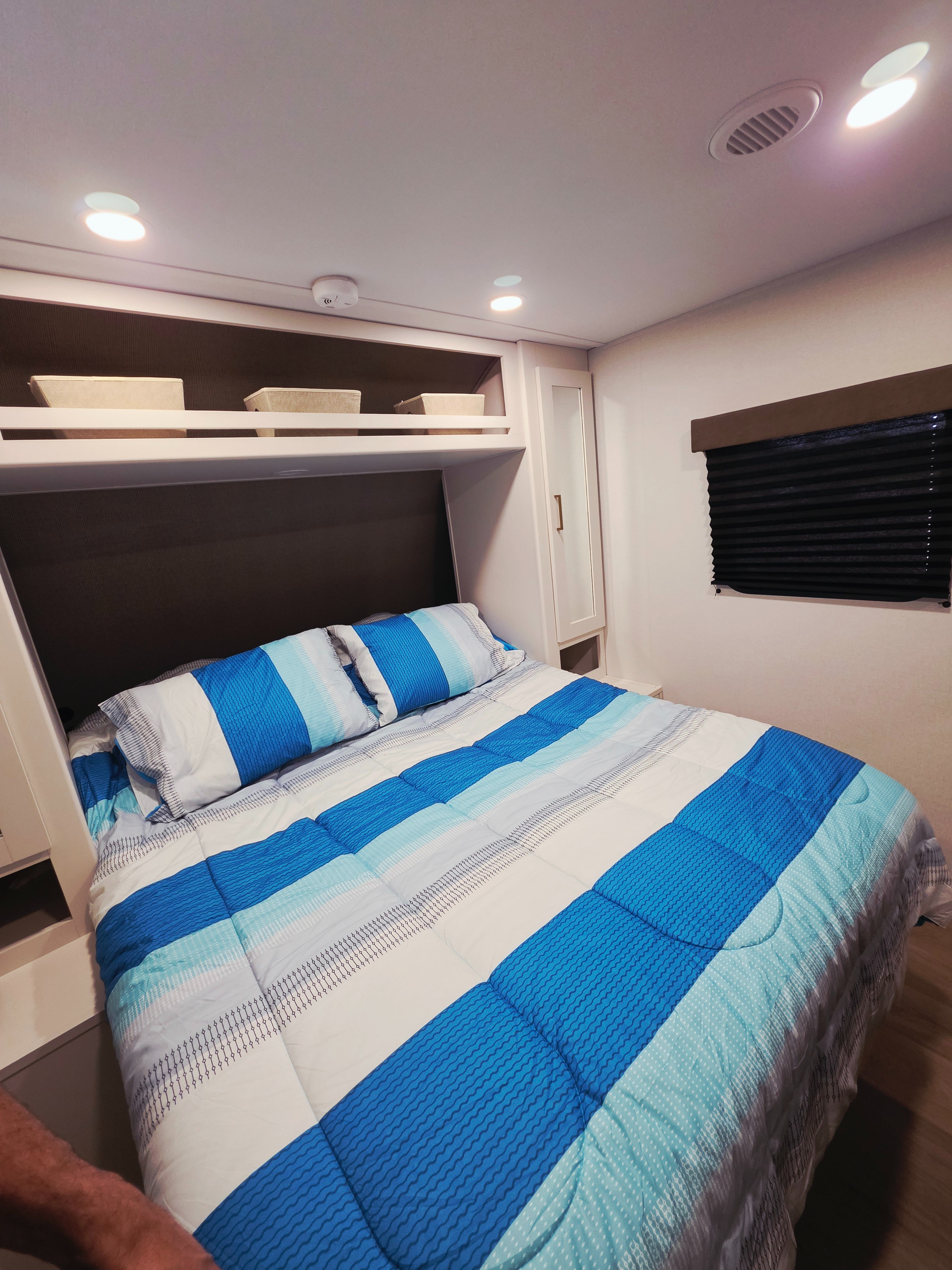 RV rental: Bedroom with blue striped bedding, overhead storage, and a window blind, offering comfortable travel.. Grand Design Transcend Xplor 26BHX 2027