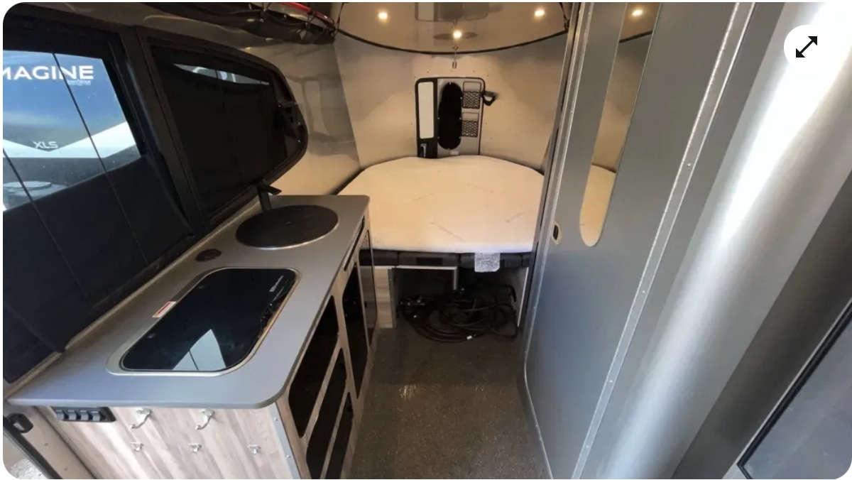 Compact rv rental interior: kitchen with stovetop/sink, cozy bed, and modern silver walls for your next adventure.. Airstream Basecamp 2023