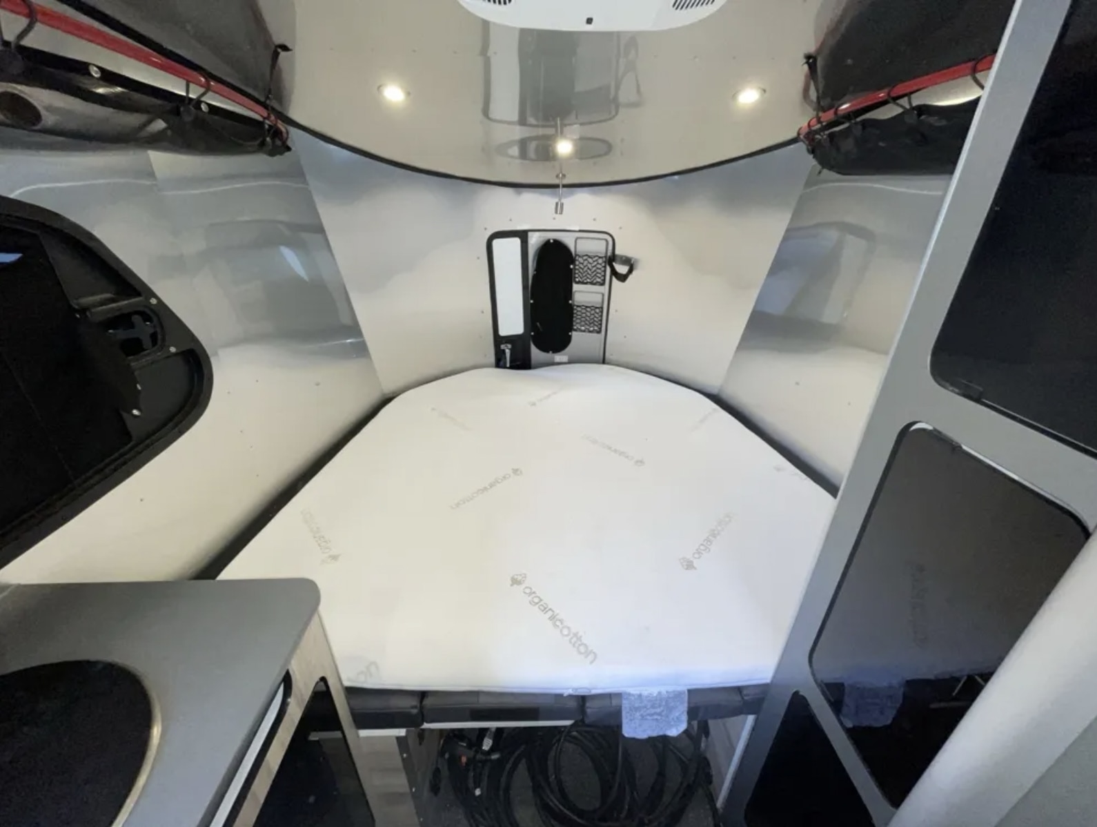RV rental's modern, compact bedroom area with an organic cotton mattress, sleek curved walls, and overhead storage.. Airstream Basecamp 2023