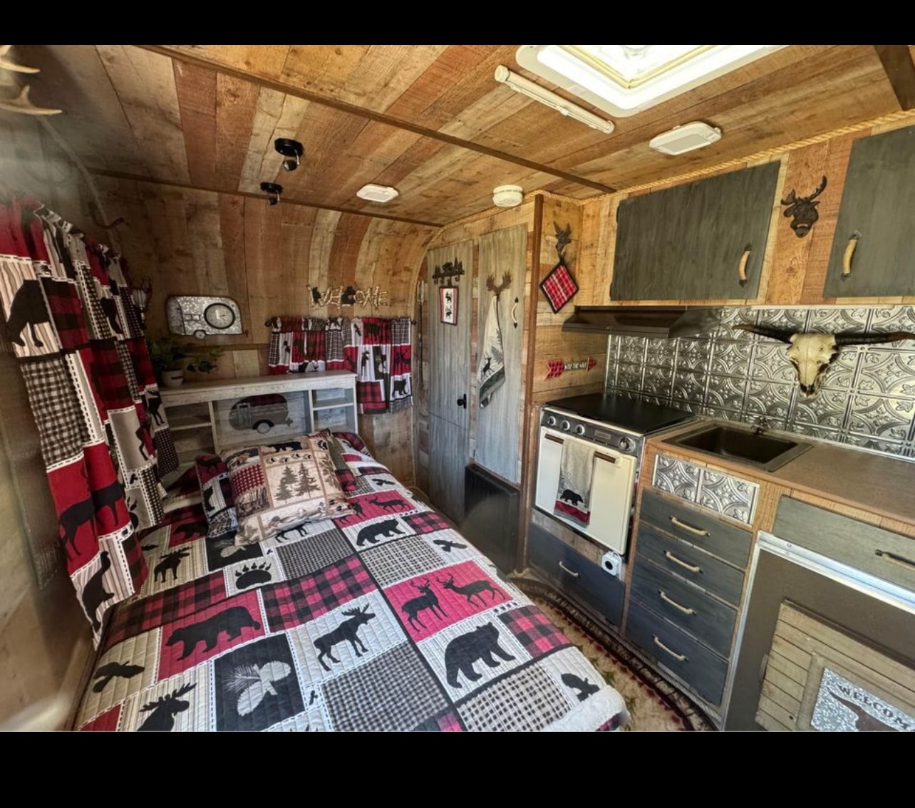 Explore this cozy, rustic RV rental! Wood-paneled interior features a plaid wildlife quilt, compact kitchen, and charming cabin decor.. Outdoors Rv Manufacturing Back Country 1970
