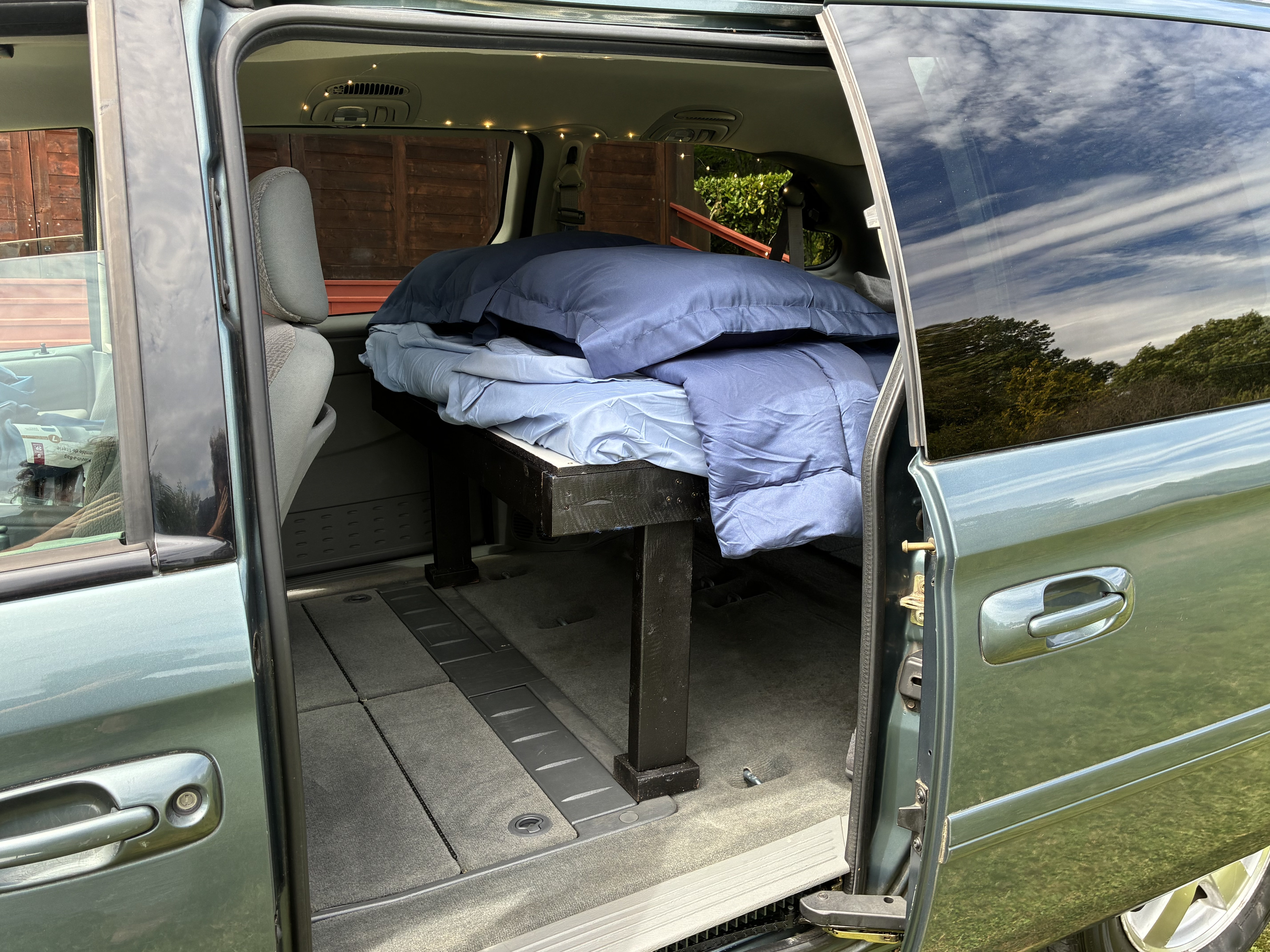 RV rental: Inside a minivan conversion with a cozy bed, pillows, and string lights, ready for van camping.. Dodge Caravan 2006