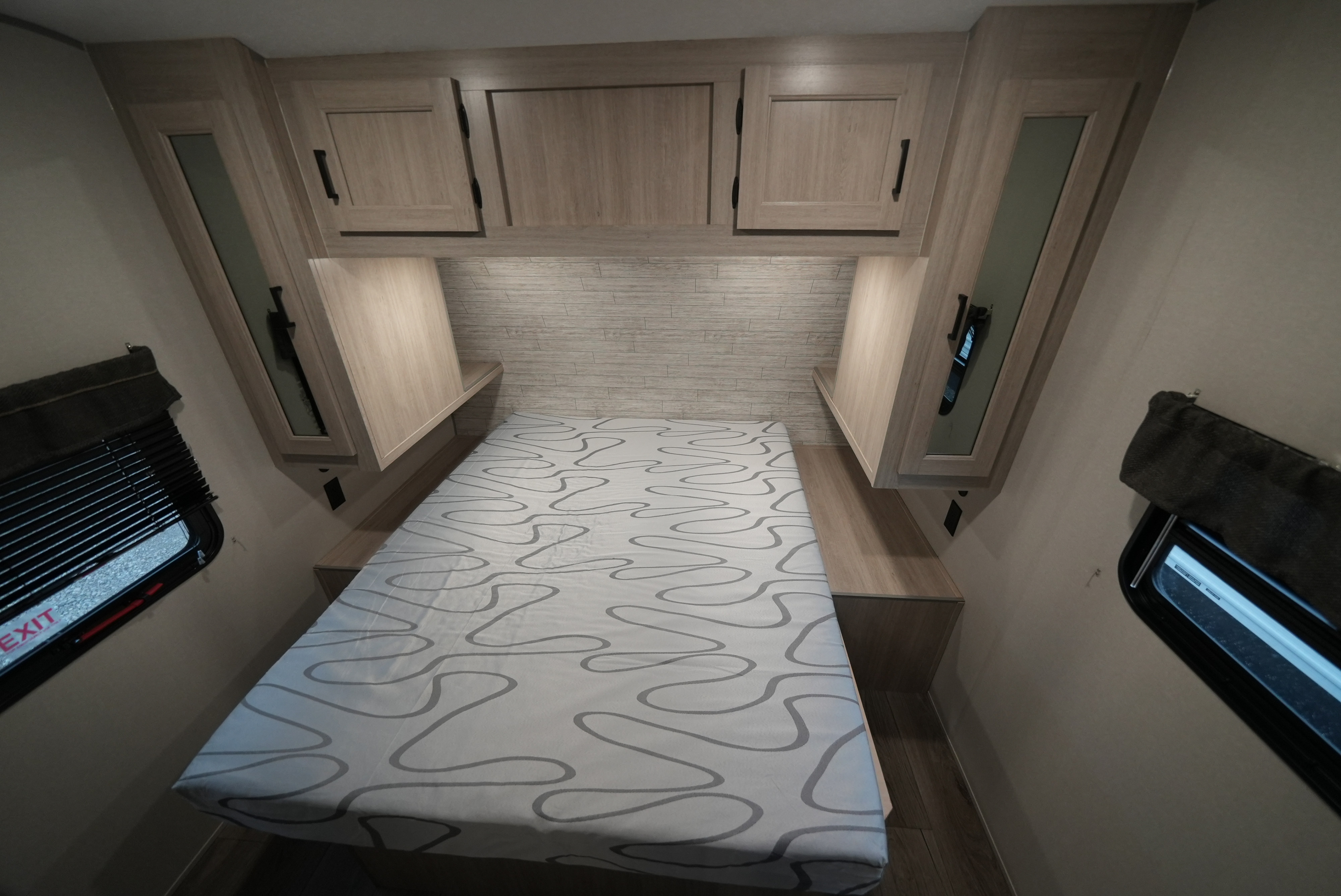 Cozy RV rental bedroom featuring a bed with a unique mattress pattern, overhead storage, and side windows with blinds.. Catalina 293TQBSCK 2025