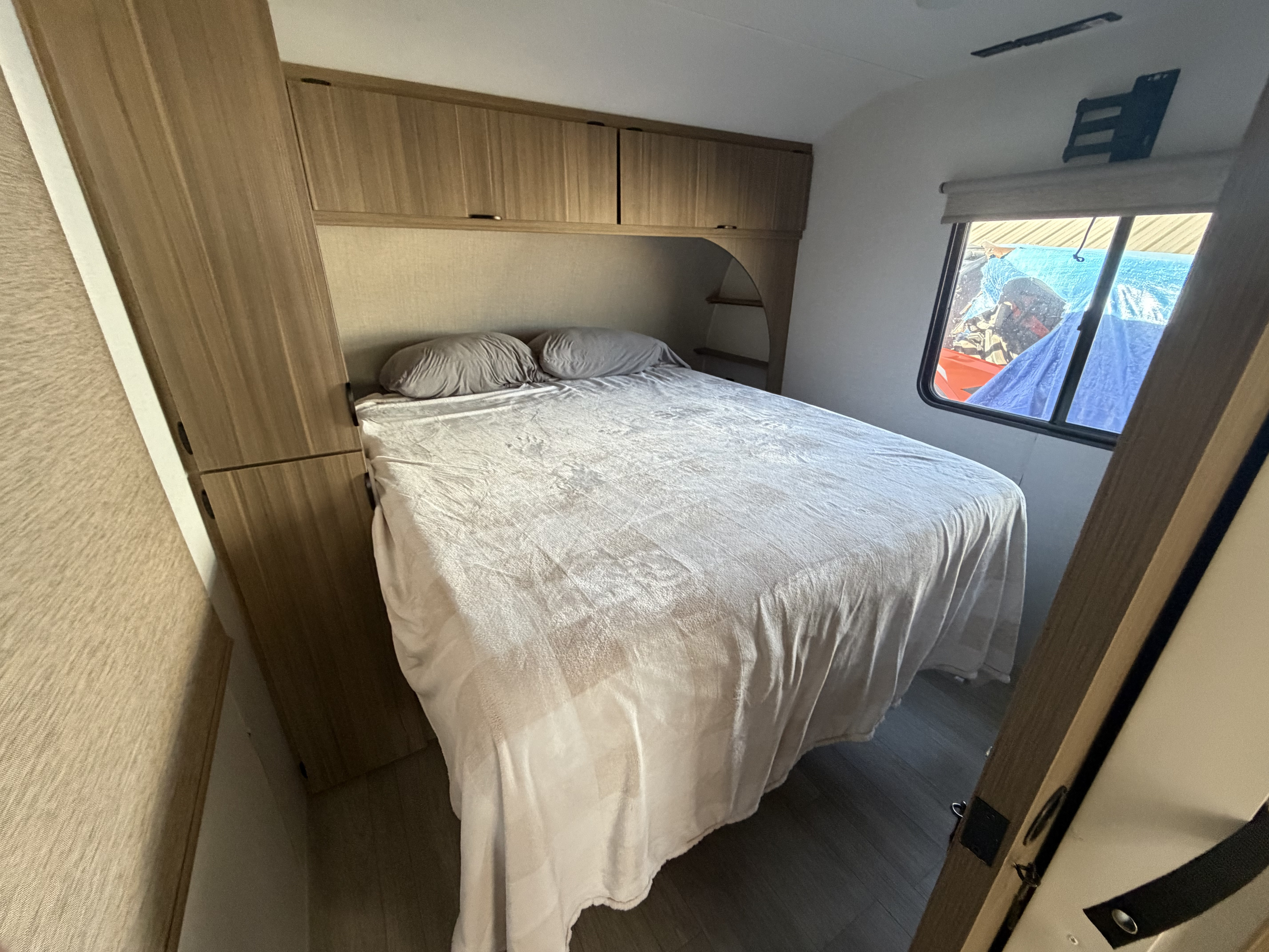 Cozy RV rental bedroom with a comfy bed, overhead storage, side cabinets, and a window for natural light.. Forest River Wildwood 2025