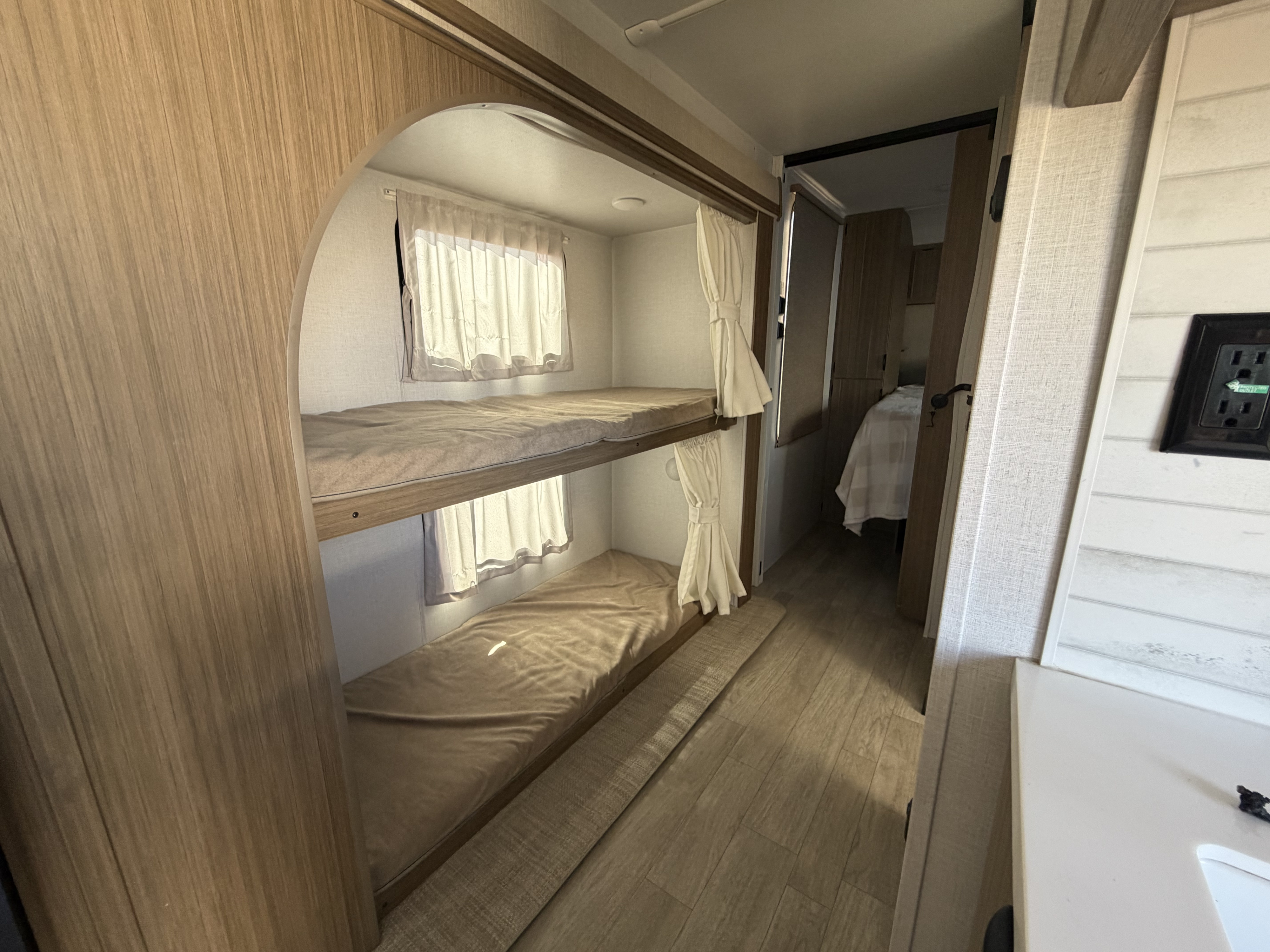 Inside an RV rental: two bunk beds with windows and curtains. The hallway leads to a main bedroom, ideal for family trips.. Forest River Wildwood 2025