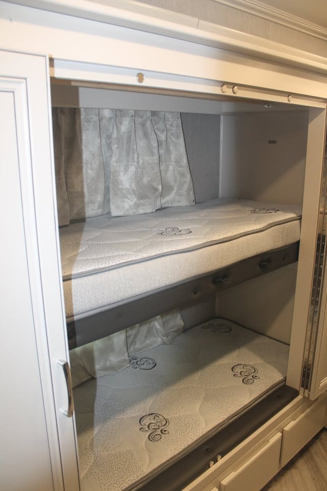 Inside an RV rental, discover built-in bunk beds with mattresses & curtains, perfect for compact sleeping.. Holiday Rambler Vacationer 2023