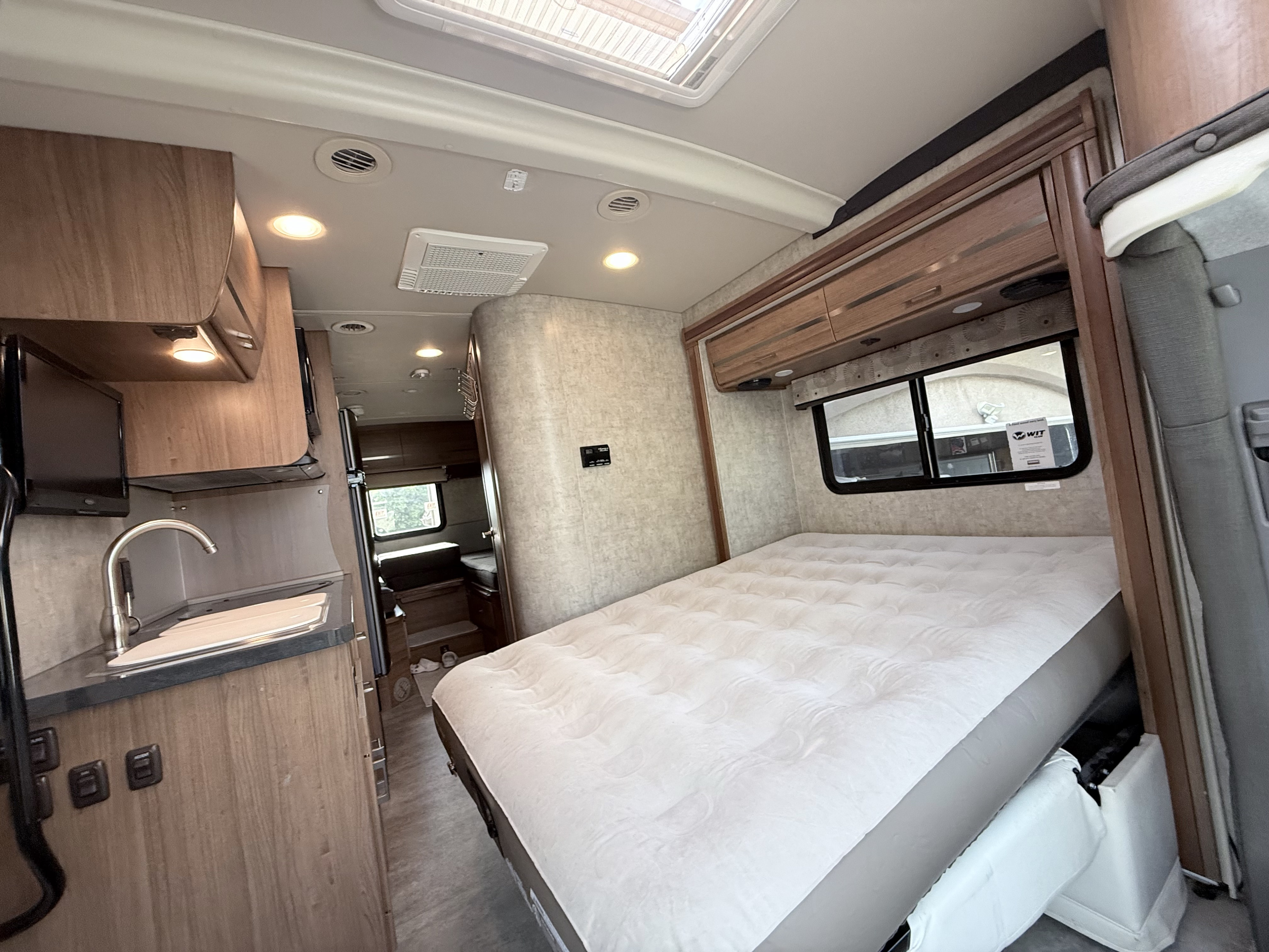 This bright RV rental interior features a plush bed, a compact kitchenette with a sink, and numerous wood cabinets.. Winnebago View 2015